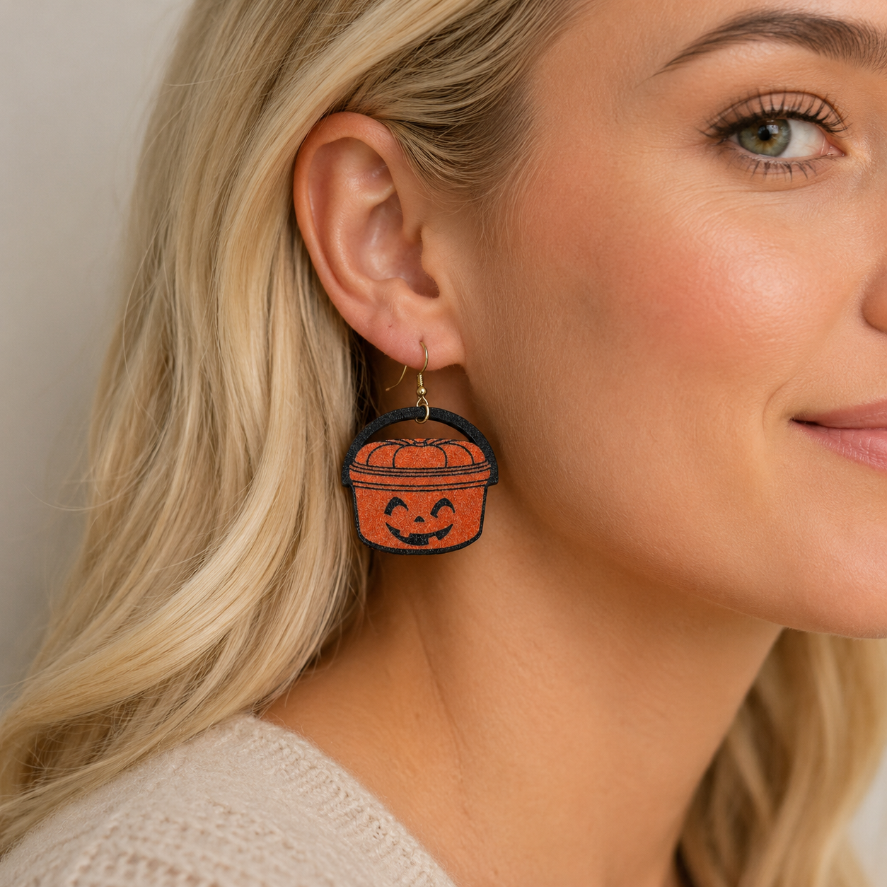 Close-up of Emma wearing an orange jack-o’-lantern pumpkin pail dangle earring showing the on-ear size and gold-tone hook.