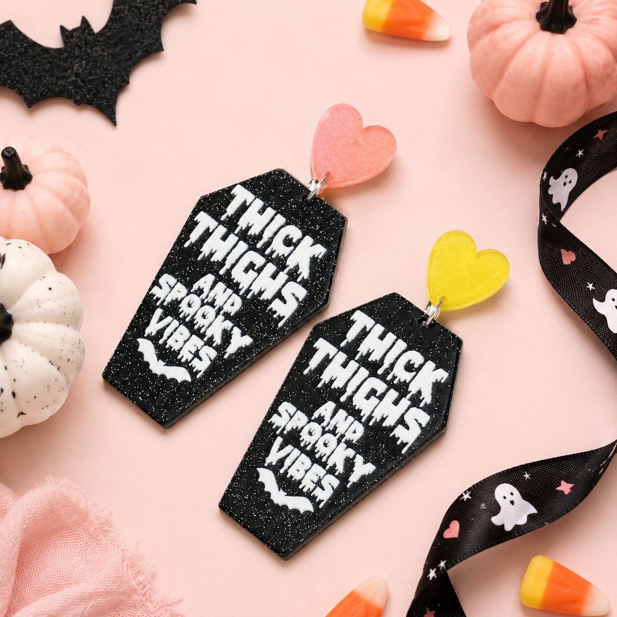 Thick Thighs & Spooky Vibes Coffin Earrings styled with pastel pumpkins, candy corn, ribbon, and Halloween accents on a blush background.