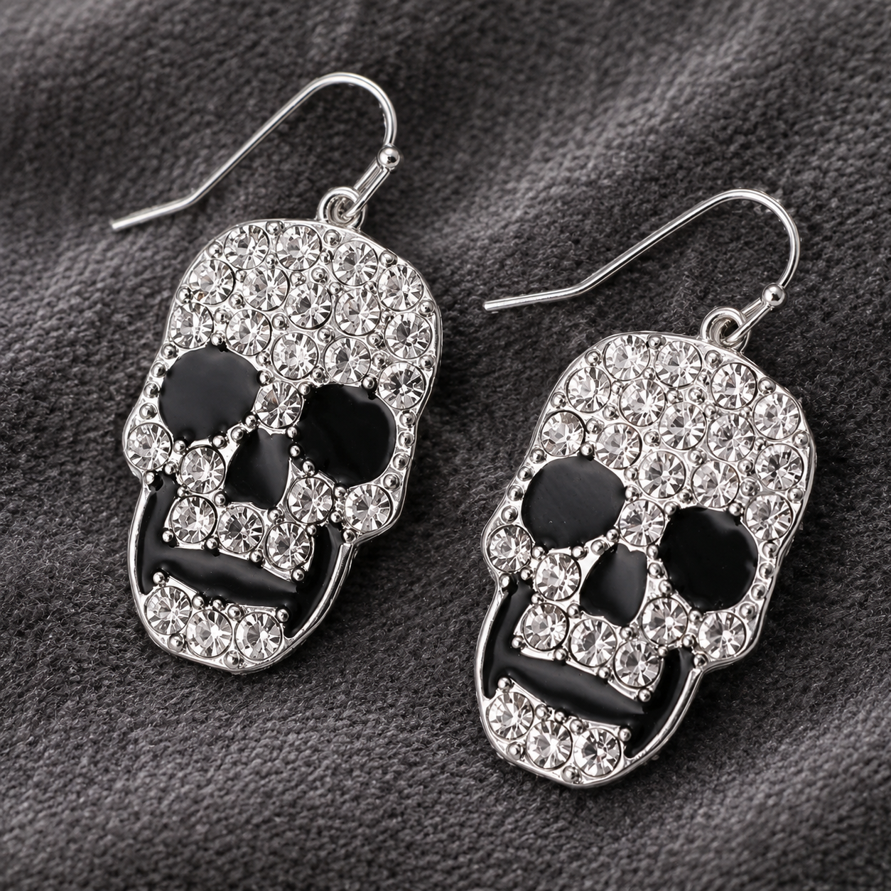 Close-up of rhinestone skull earrings with black enamel details styled on charcoal fabric