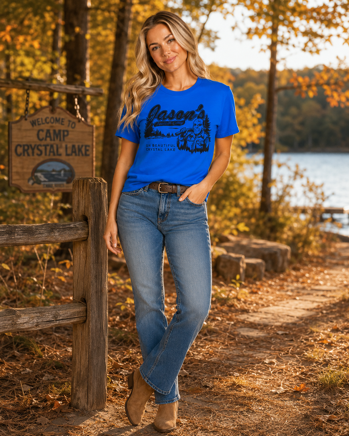 Emma wearing Crystal Lake Camp royal blue tee outdoors beside a lake during golden hour