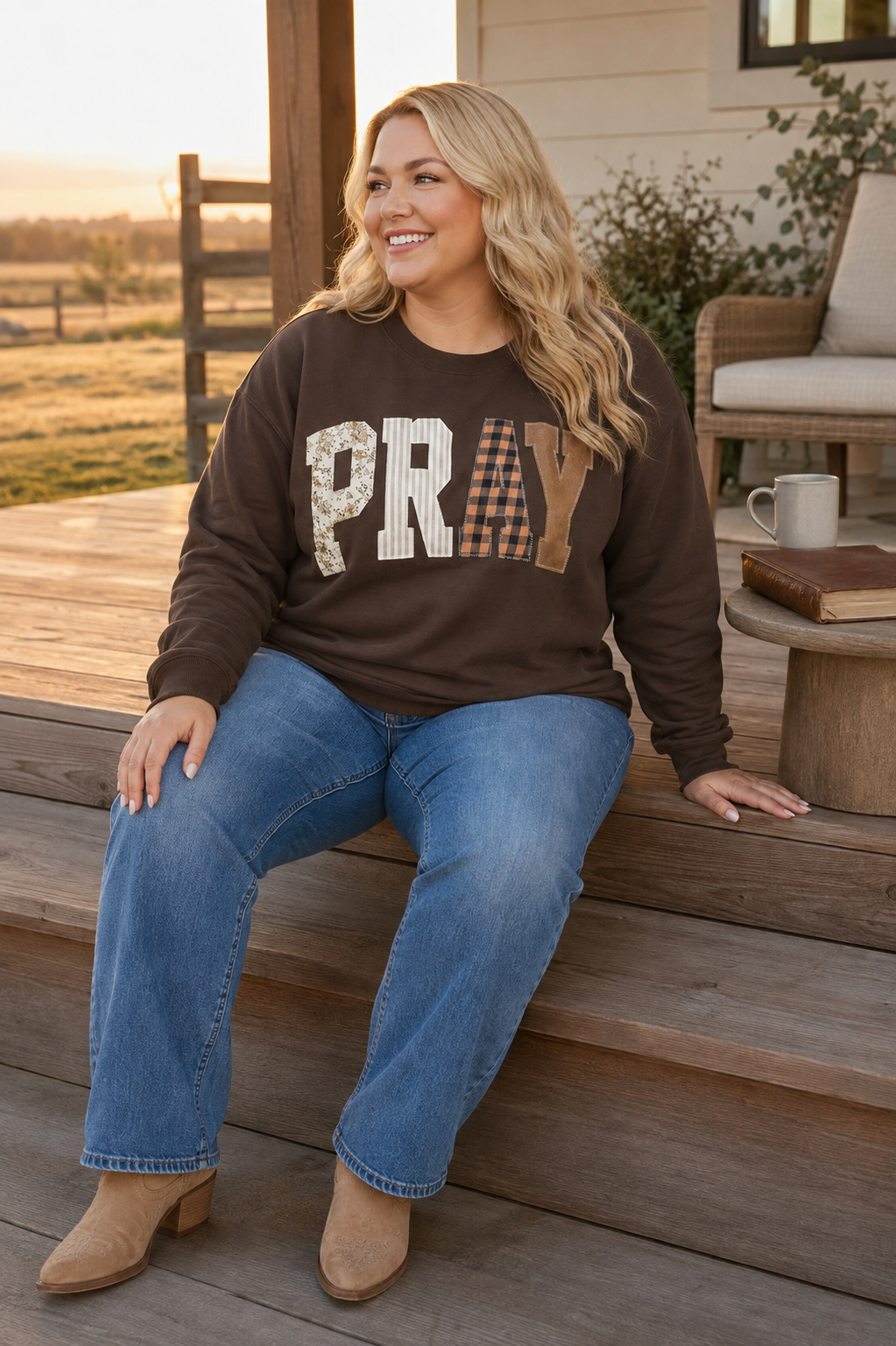 Plus-size woman wearing a coffee-brown PRAY patchwork sweatshirt during a peaceful sunrise devotional on a ranch-house porch.