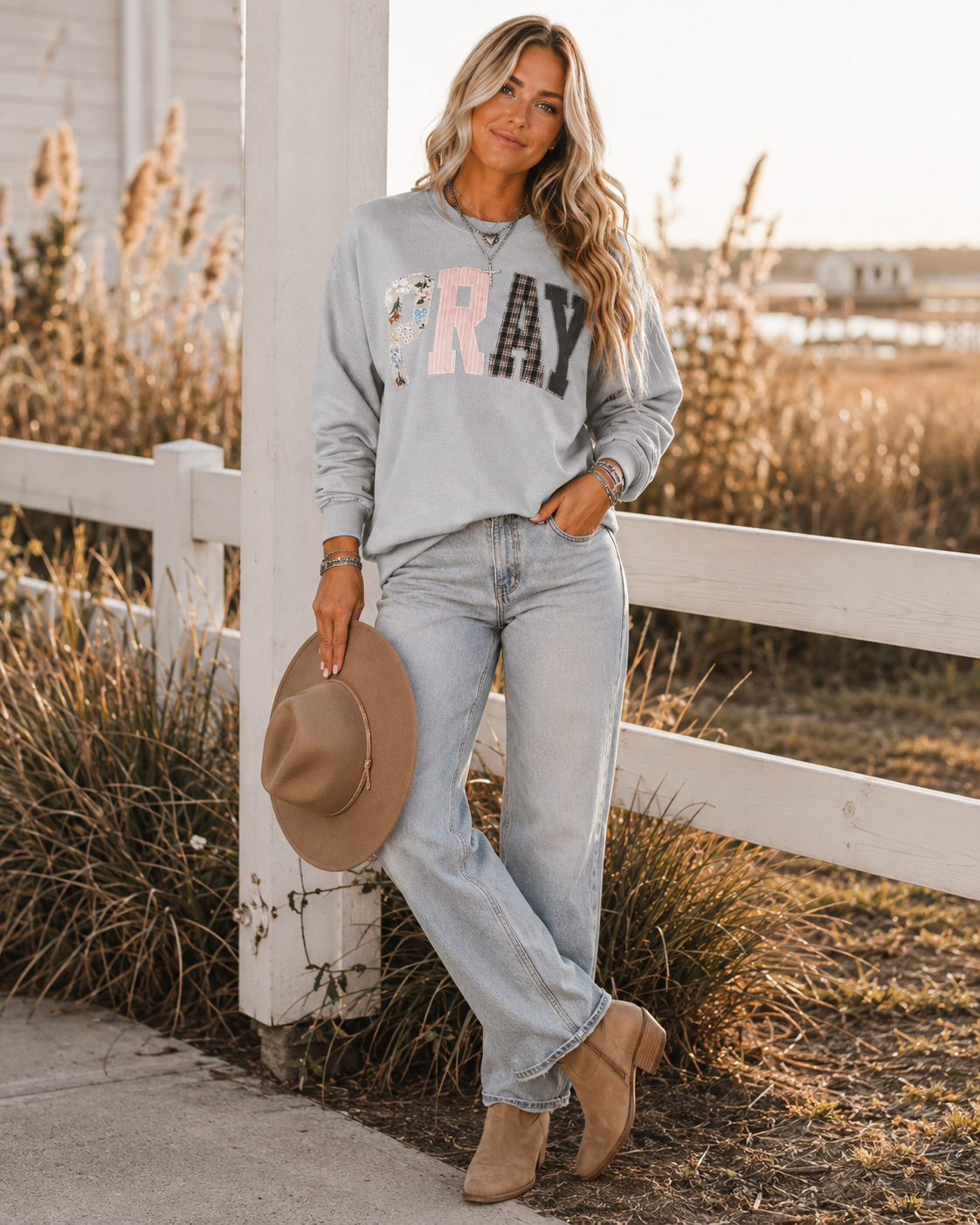 Emma wearing the gray Pray Through It sweatshirt with light wash denim and boots outdoors at golden hour.