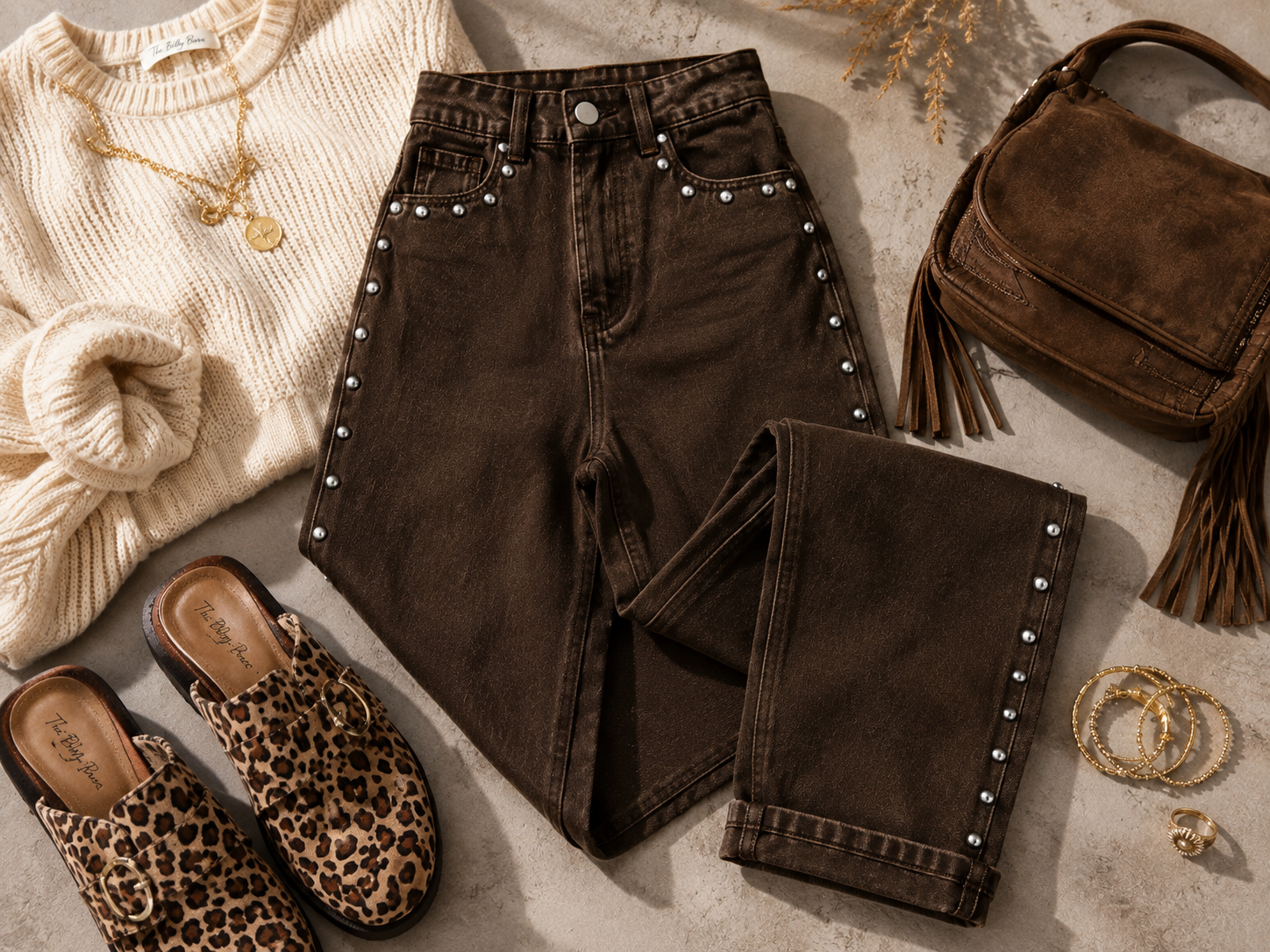 Flat lay of coffee brown Saddle Stud Jeans styled with an ivory sweater, leopard mules, brown handbag and gold jewelry.
