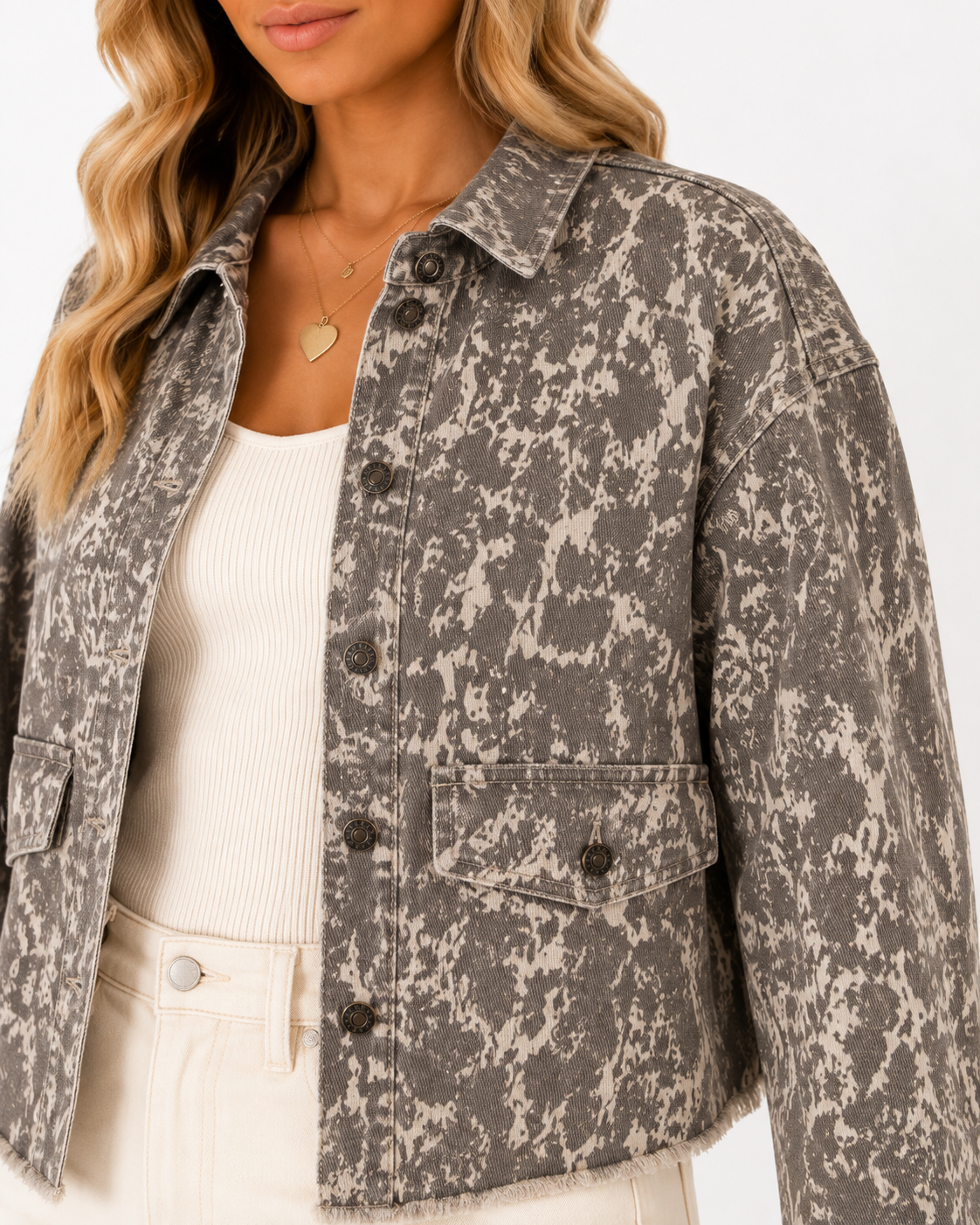 Close-up of the Dust & Stone denim jacket showing the abstract khaki and charcoal print, pointed collar, metal buttons, chest pocket and raw hem detail.