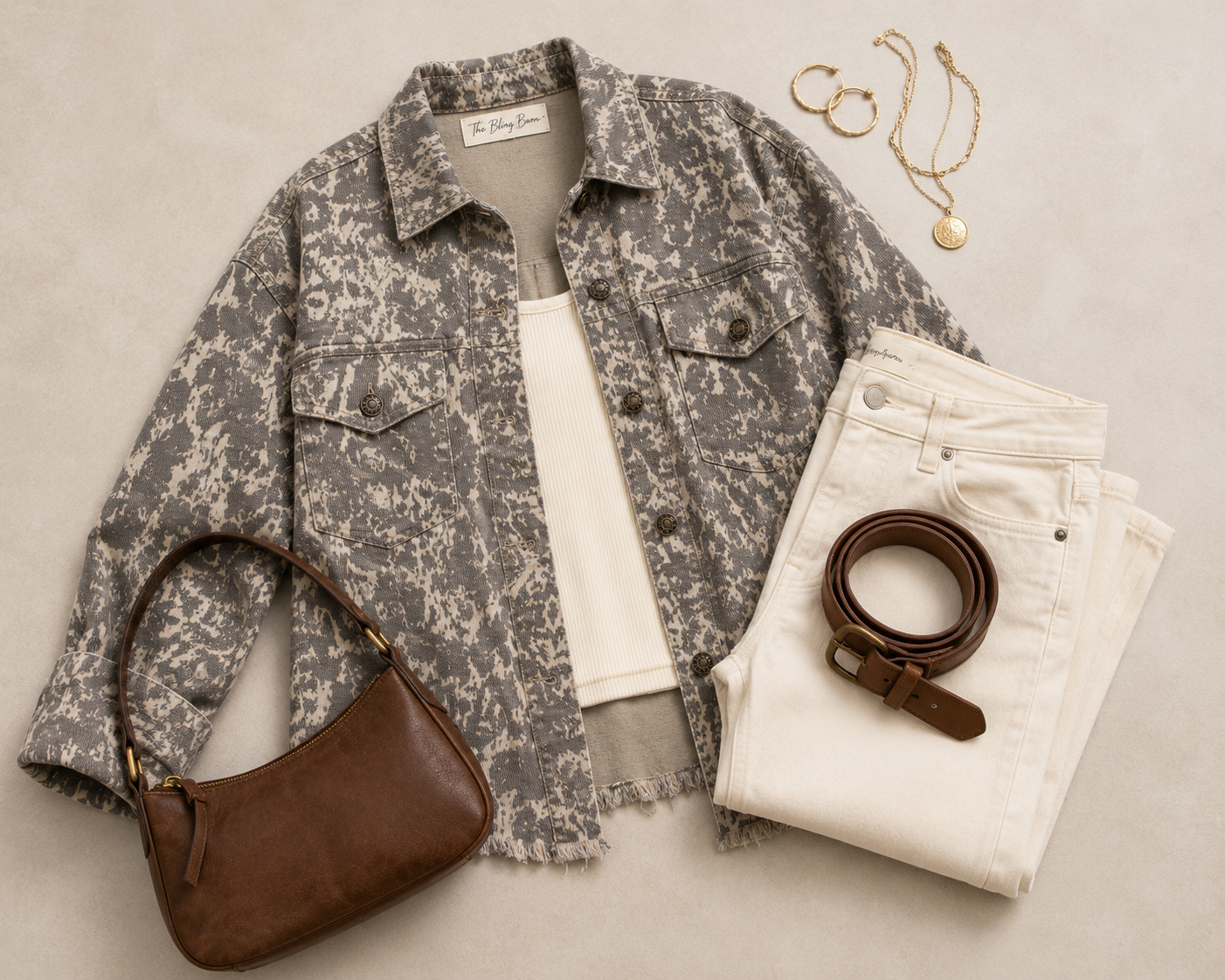 Flat lay of the Dust & Stone Abstract Denim Jacket styled with an ivory tank, cream jeans, brown belt, handbag and gold jewelry.