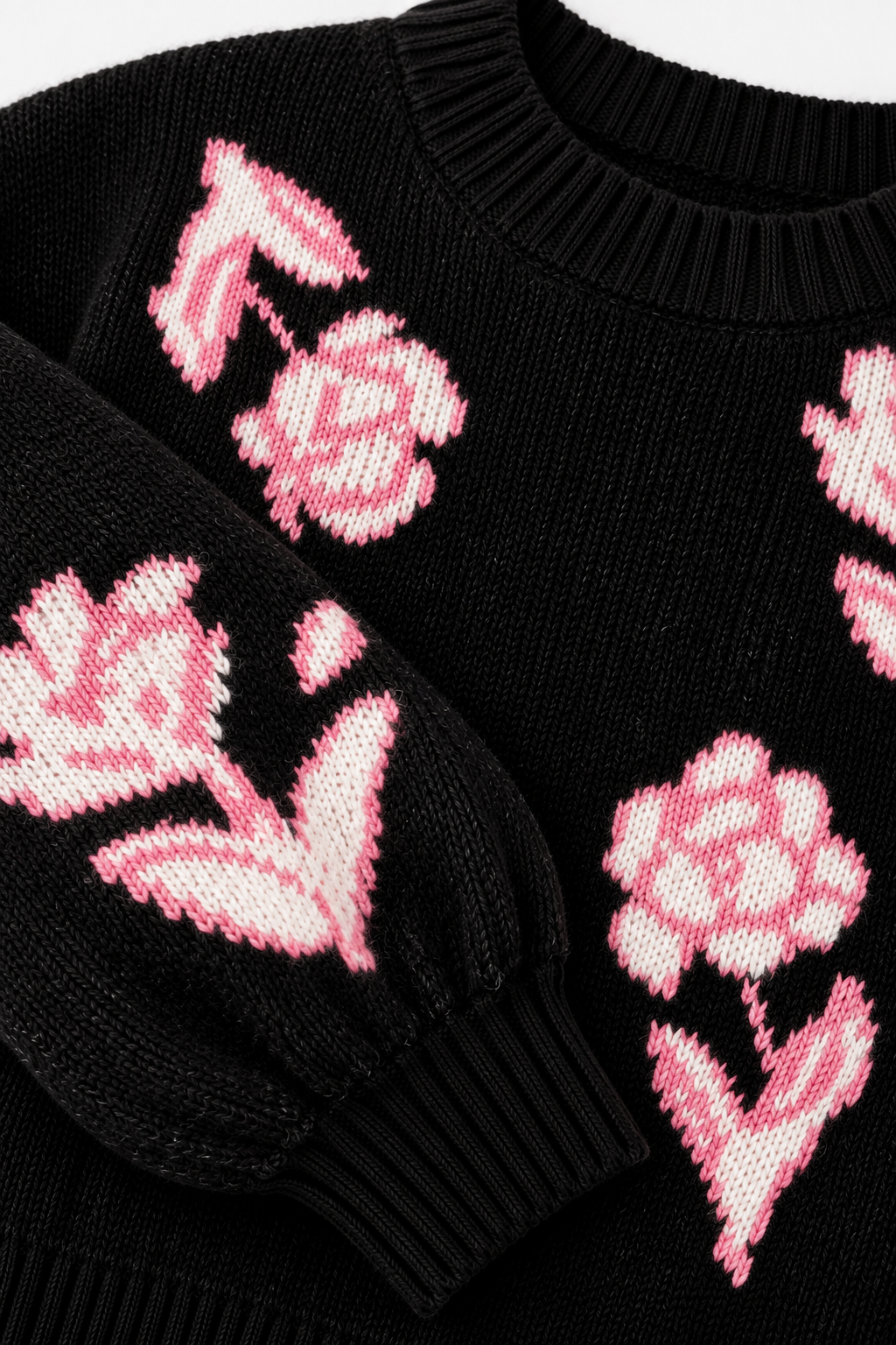 Close-up of a black knit sweater with pink knitted floral motifs, including tulips and roses, on the chest and sleeve.