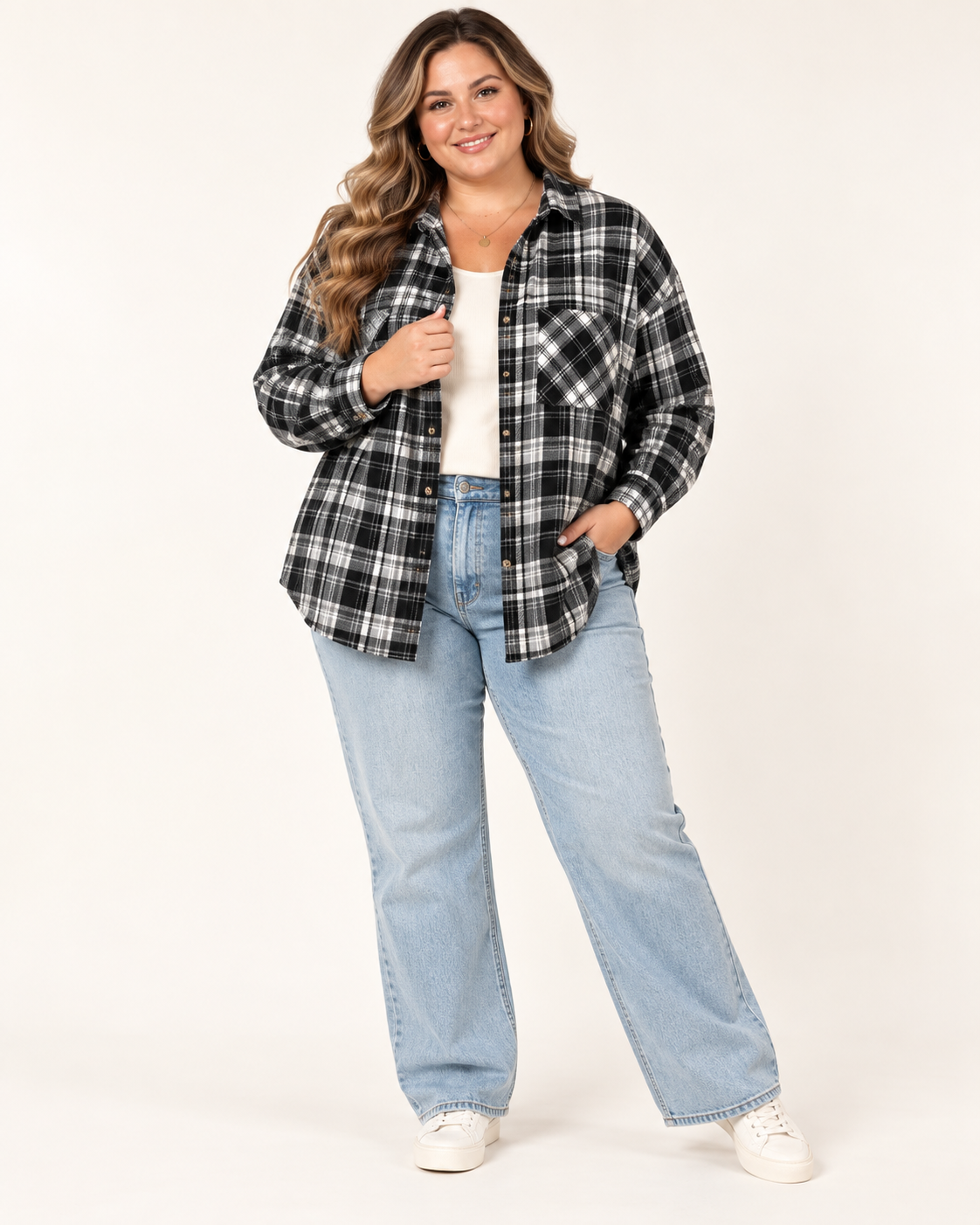 A woman modeling a black and white plaid button-down flannel shirt over a white top, paired with light-wash blue jeans and white sneakers, against a plain off-white studio background.