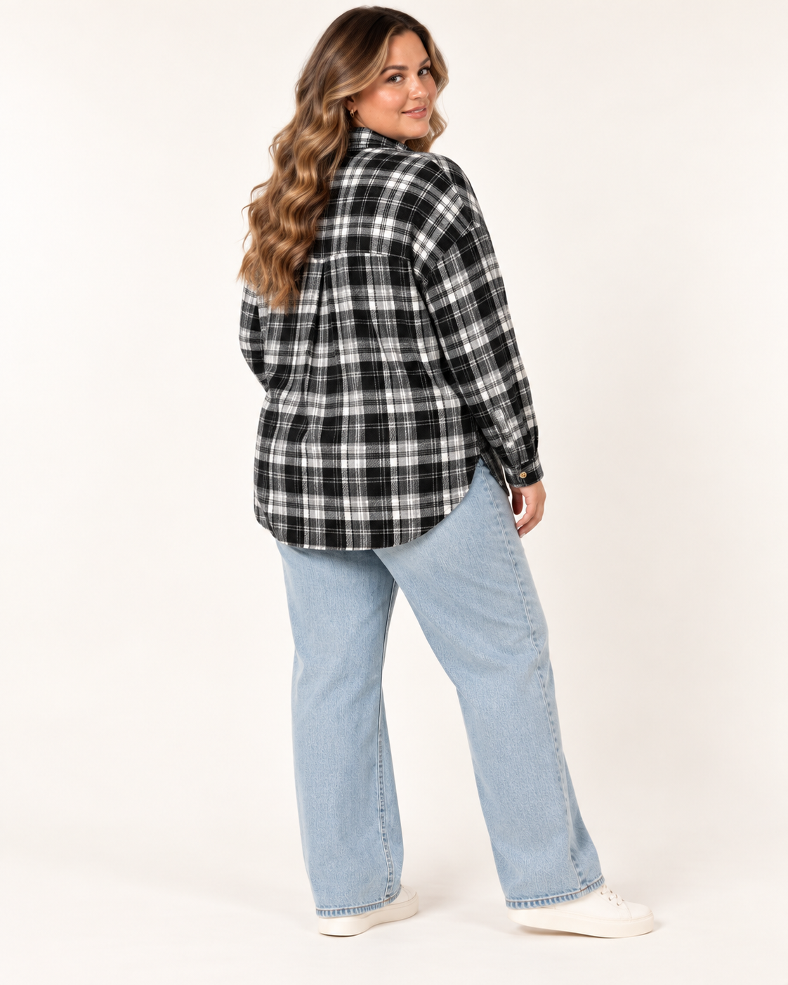 A woman modeling a black and white plaid flannel shirt with light blue jeans and white sneakers, photographed from the back against a plain off-white studio background.