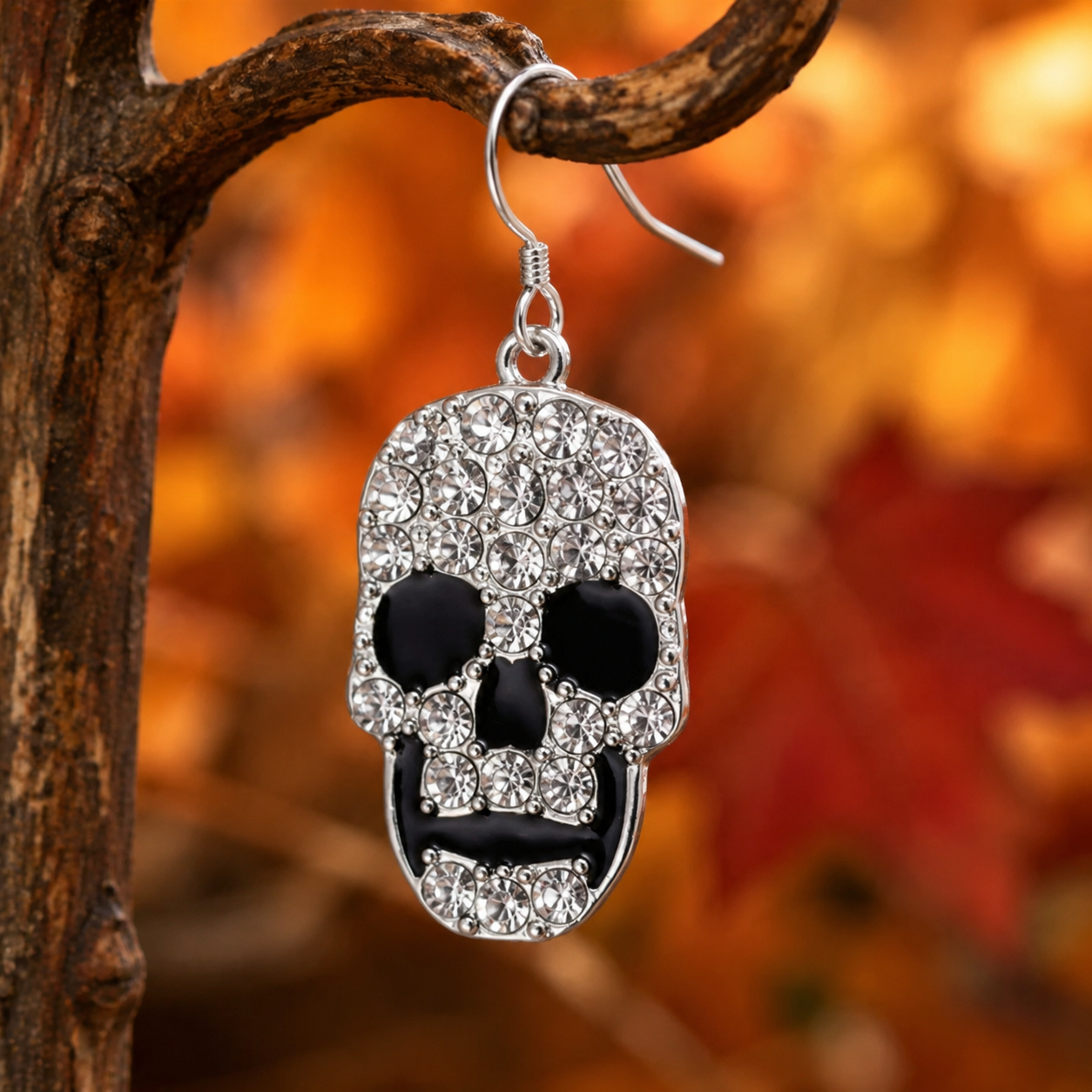 Close-up of crystal skull earring hanging against glowing orange autumn leaves