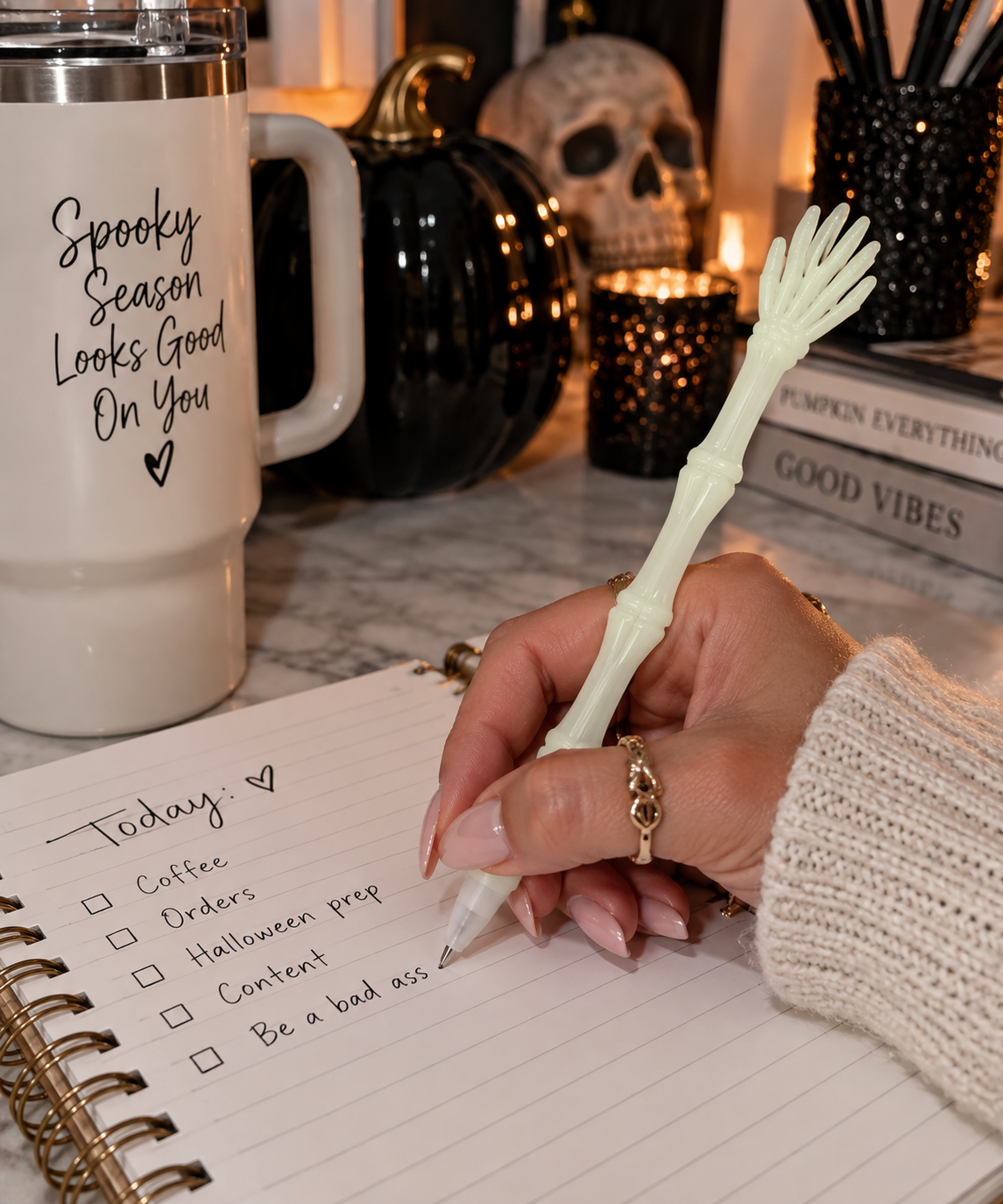 Skeleton hand pen styled on a rustic desk beside spooky decor and a black skull