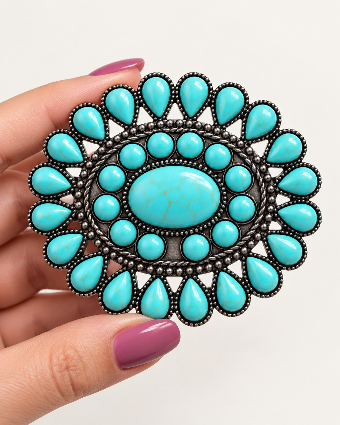 a large oval silver-toned brooch featuring a central turquoise cabochon and surrounding turquoise teardrop and round stones.