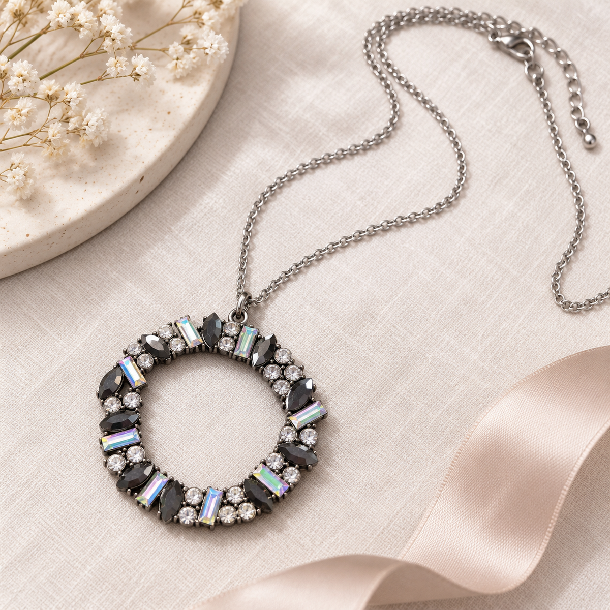 Iridescent crystal wreath necklace styled on soft neutral linen with blush satin ribbon and delicate floral accents