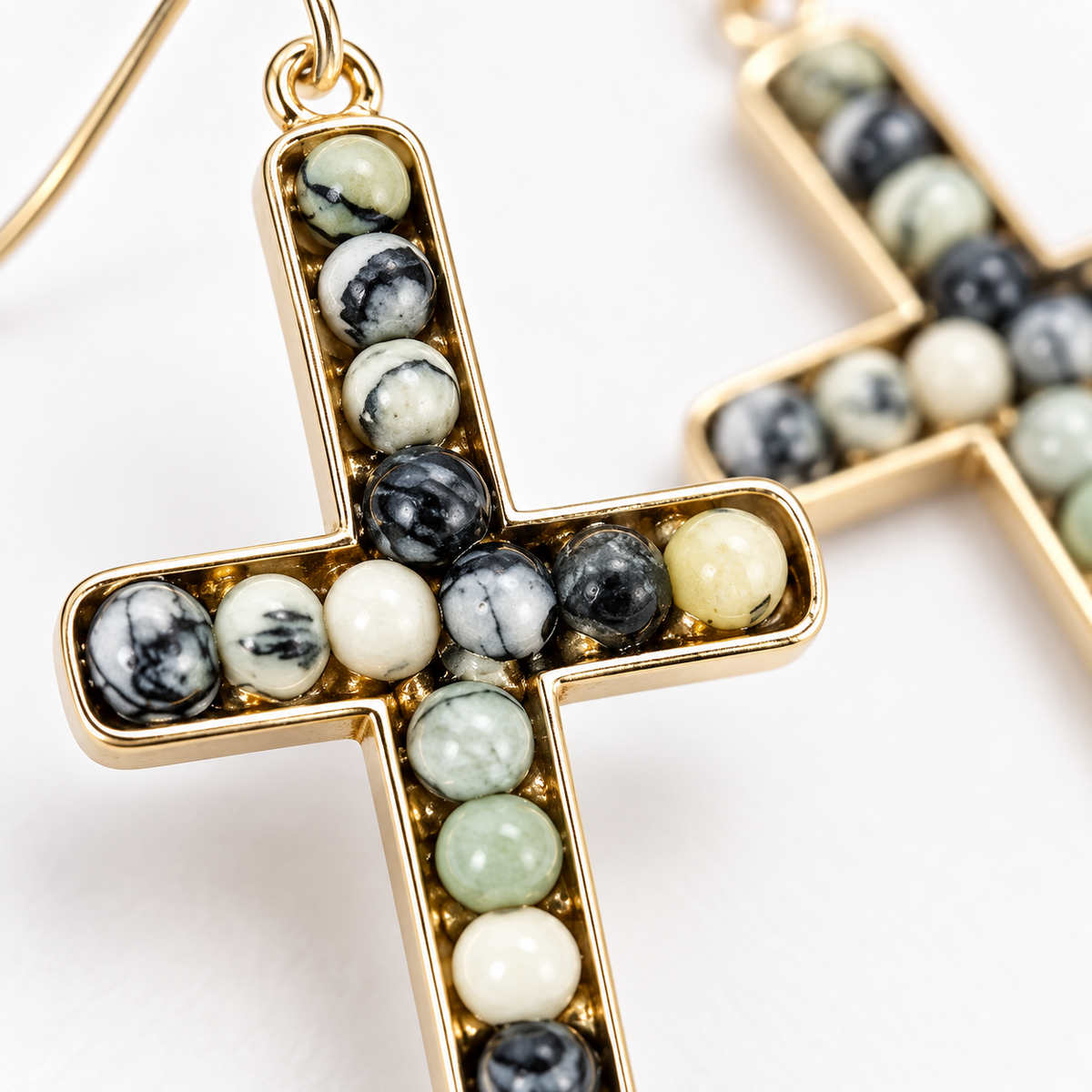 Gold cross pendant earrings featuring inlaid round beads in black, white, and light green marbled stone, shown in a close-up studio shot.
