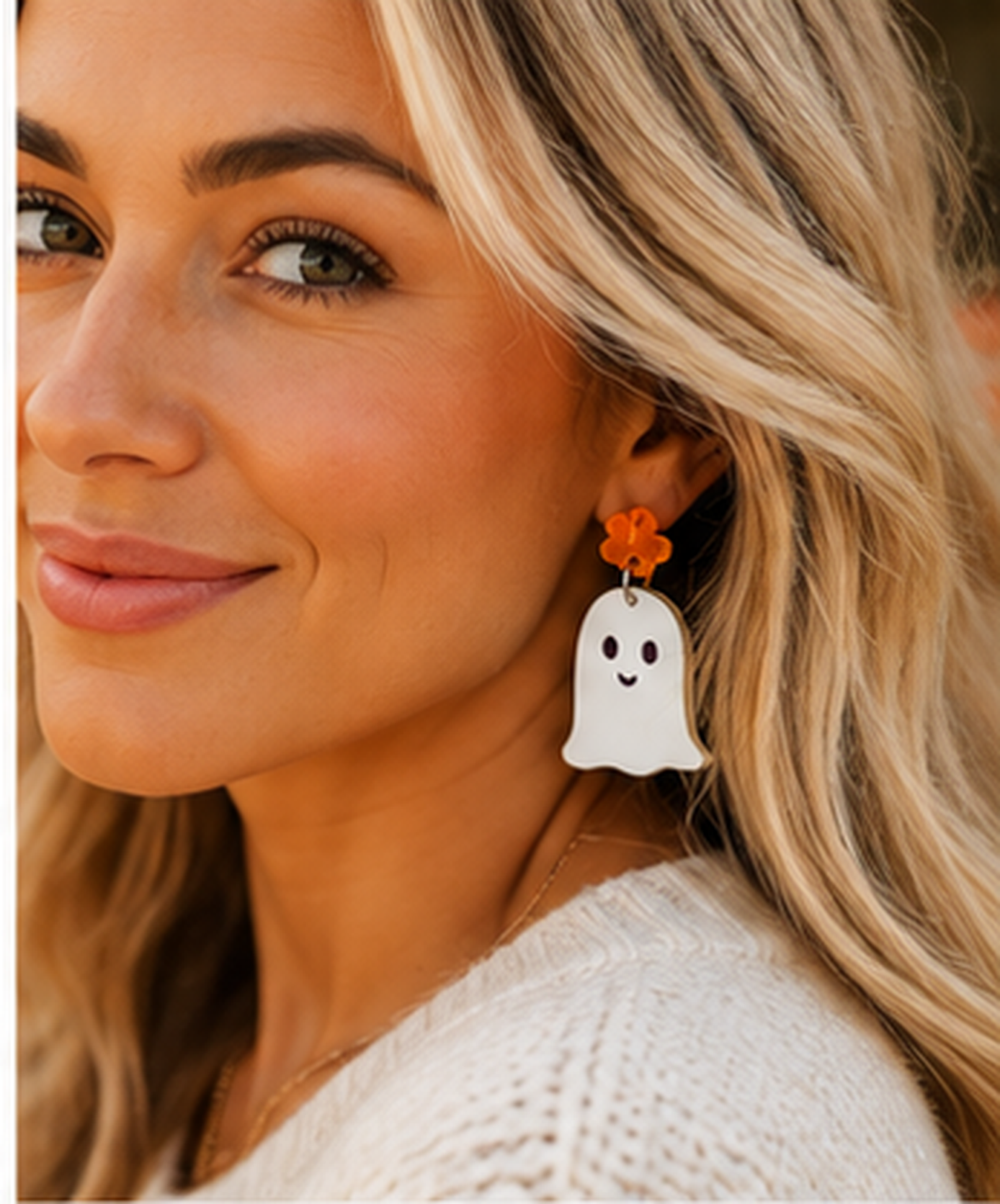 A close-up lifestyle shot of a woman wearing a white ghost-shaped dangle earring with a small orange flower accent at the top.