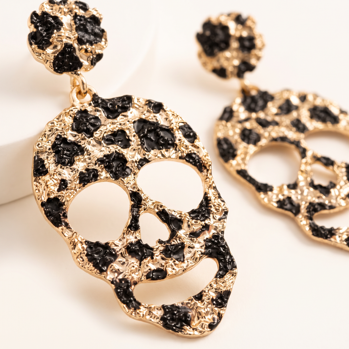 Gold-tone skull drop earrings with black textured stone accents, shown in a close-up studio shot on a light background.