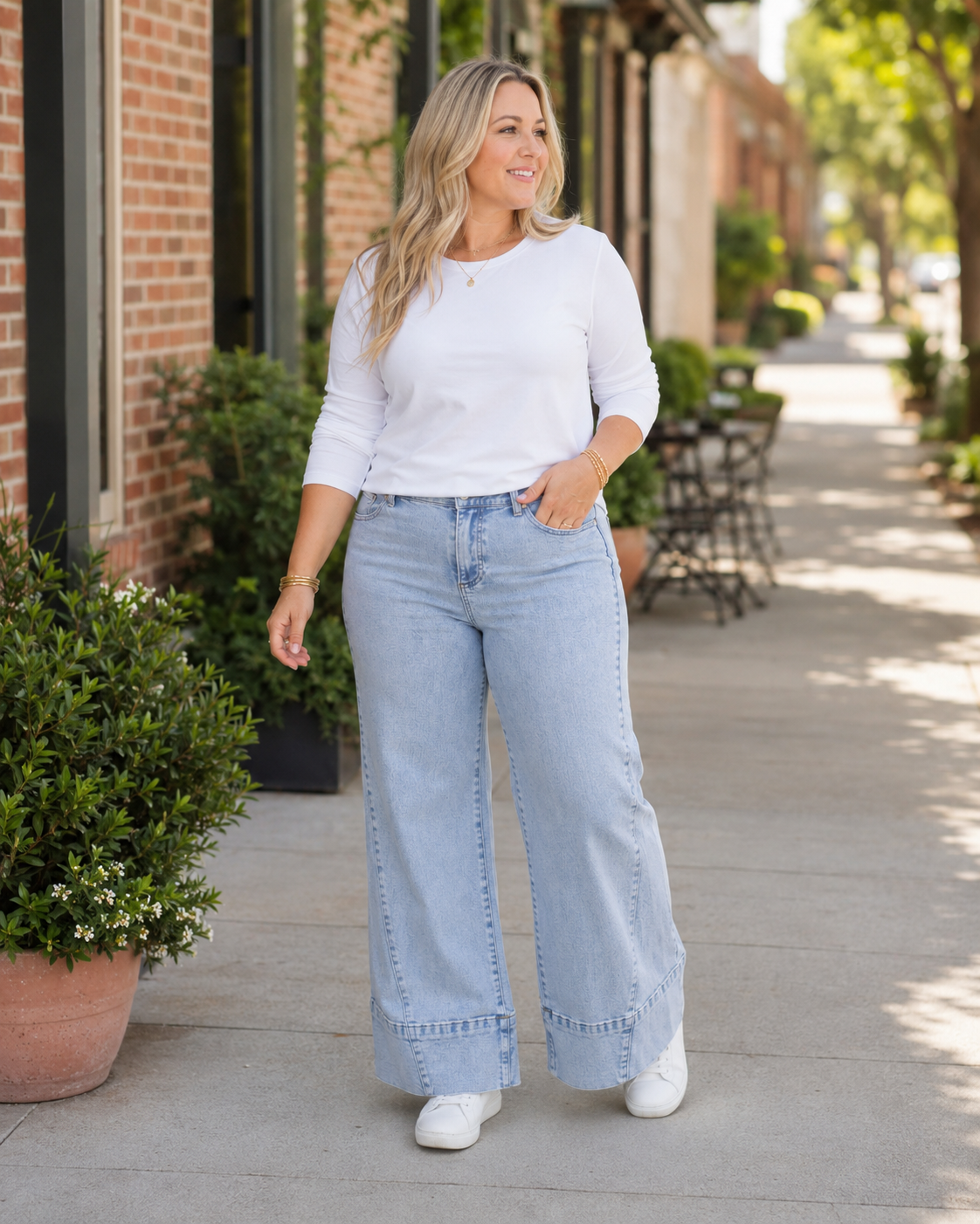 Blonde model wearing Beau Blue Seamed Wide-Leg Plus Size Jeans with a white top and sneakers on a sunlit shopping street
