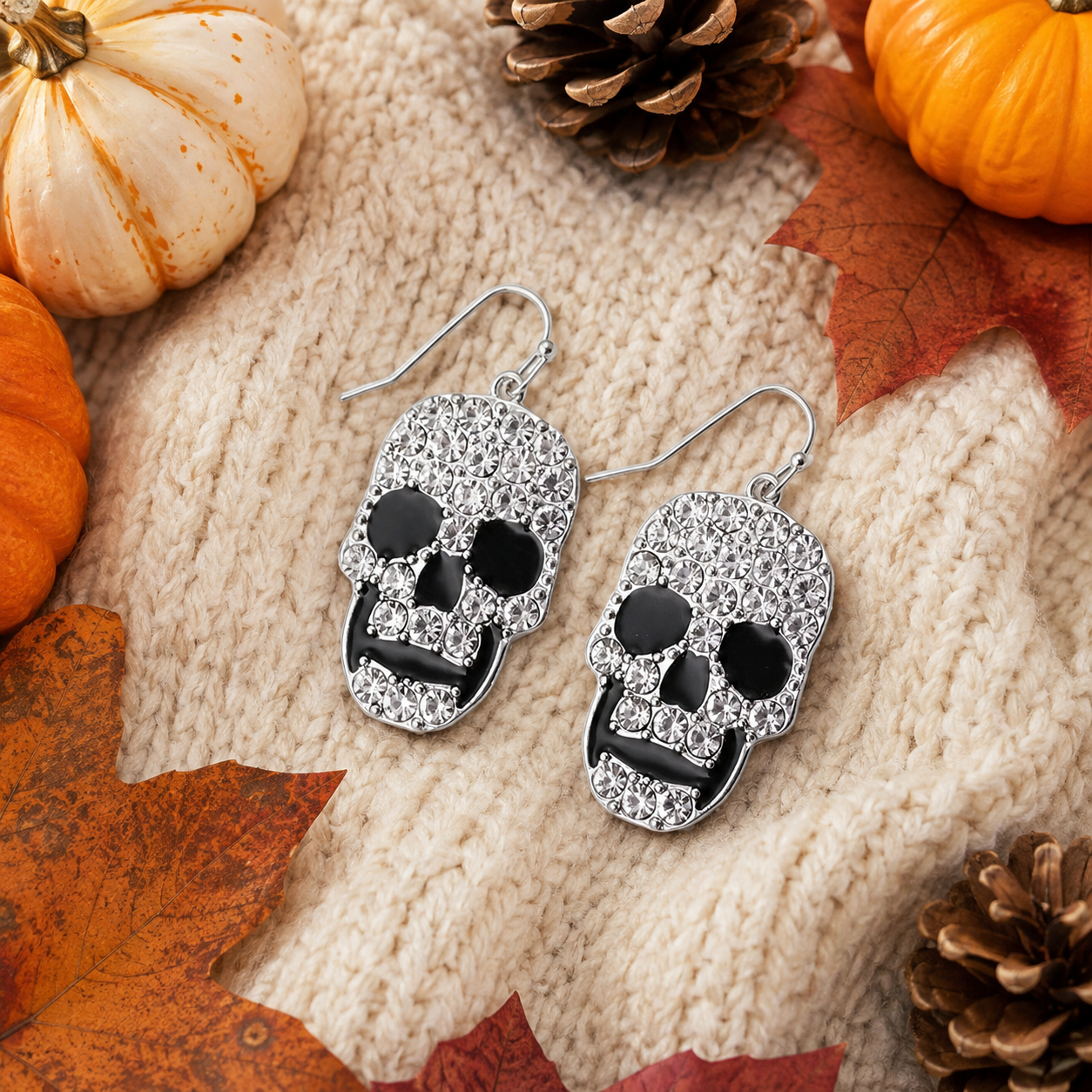 Midnight Skull Rhinestone Earrings styled on cream knit with pumpkins, pinecones and fall leaves