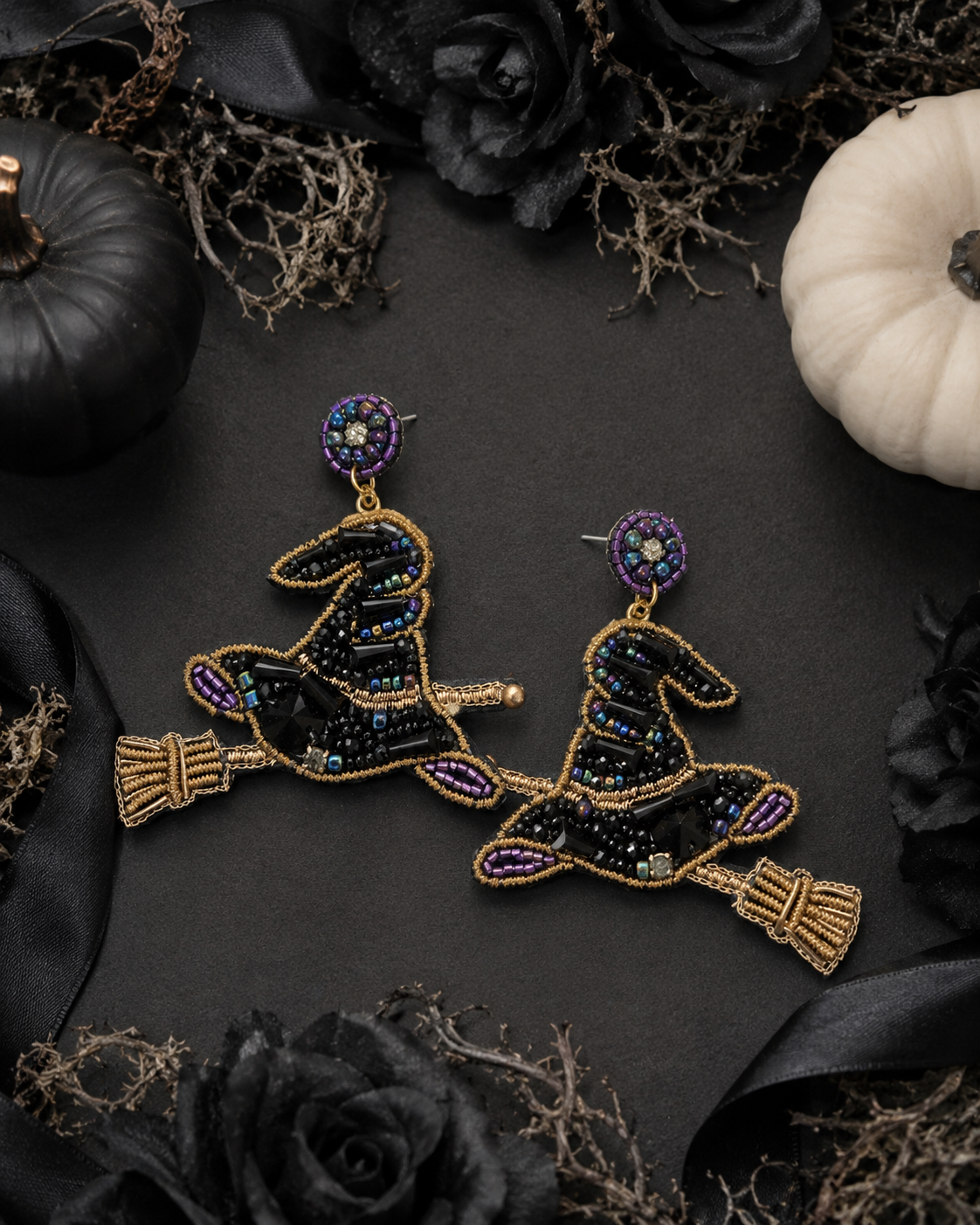 Beaded witch hat earrings styled with black roses, ribbon and Halloween pumpkins on a dark background