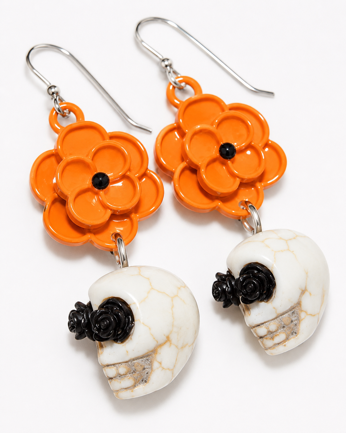 Close-up of orange flower and ivory skull earrings showing black rose eye accents and crackle detailing