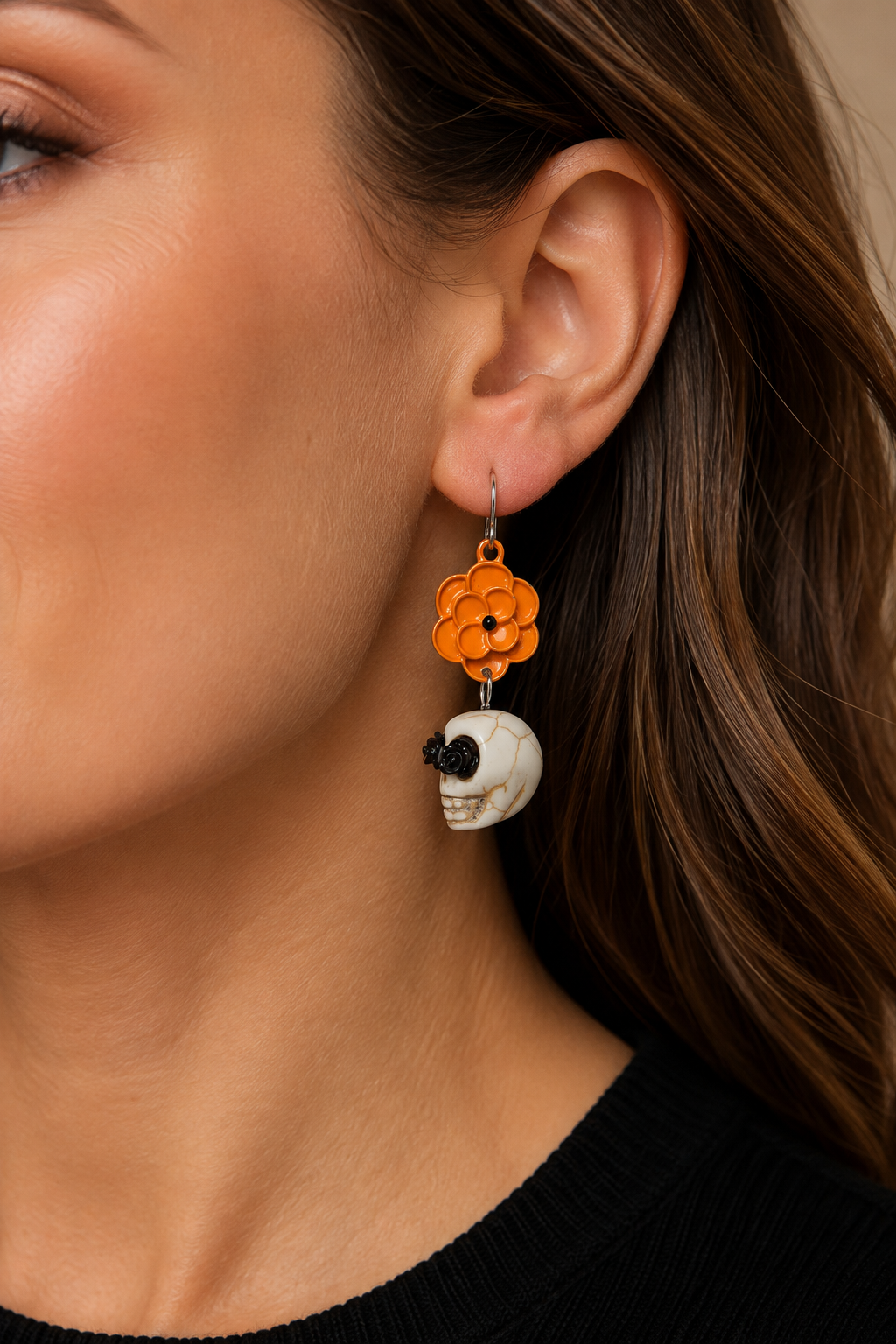 Woman wearing orange flower and skull Halloween earrings with a black top in a warm autumn setting