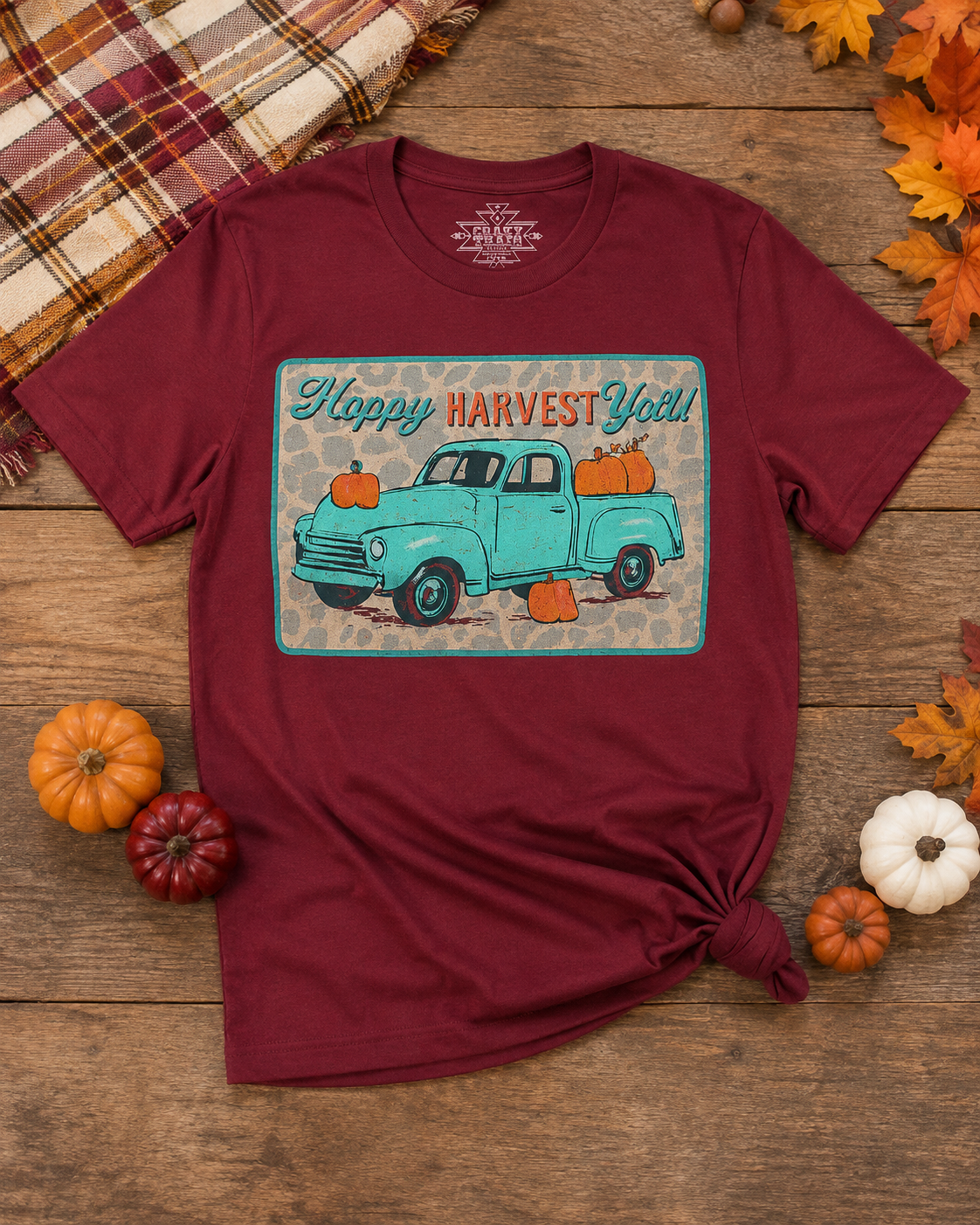 Harvest Roads fall graphic tee laid flat with pumpkins, autumn leaves and plaid accents on a rustic wood background