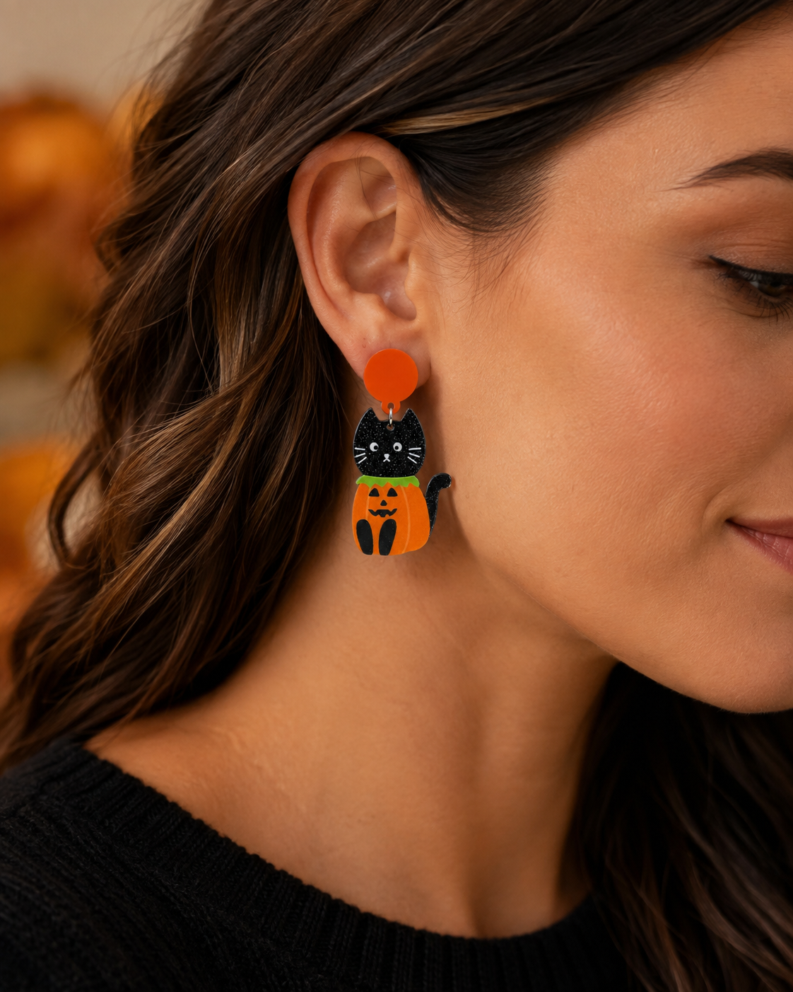 Close-up of woman wearing black cat and pumpkin Halloween statement earrings