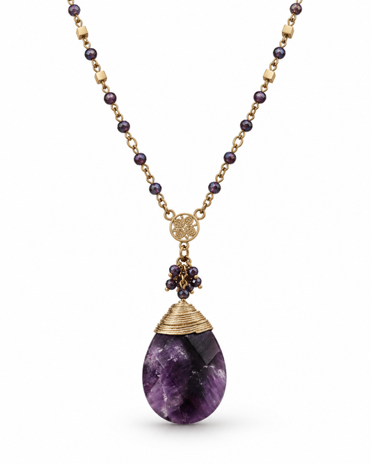 A gold-tone necklace featuring a teardrop-shaped purple amethyst pendant, a gold wire-wrapped cap, and a cluster of small dark purple beads, shown against a plain white background.