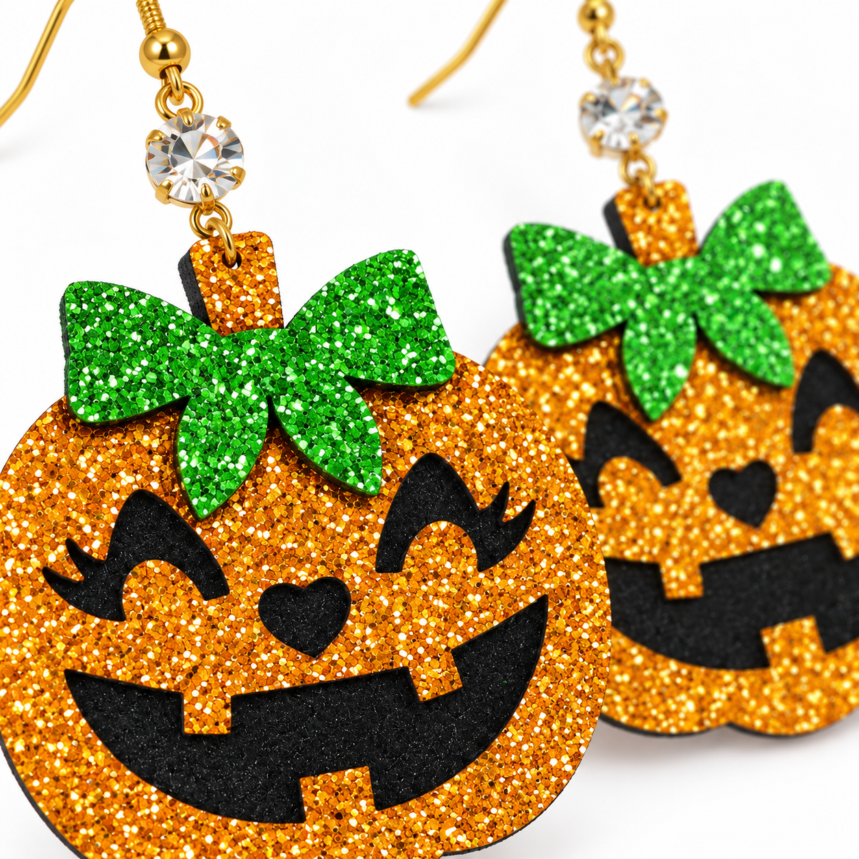 Glittery orange jack-o'-lantern earrings with green bow accents and gold-tone hooks on a white background.