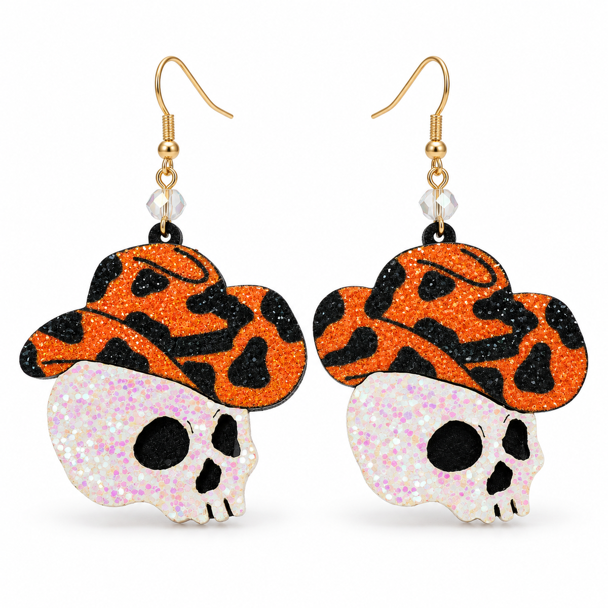 A pair of dangling earrings featuring glittery orange and black patterned cowboy hats with white glitter skulls underneath, suspended from gold hooks on a white background.