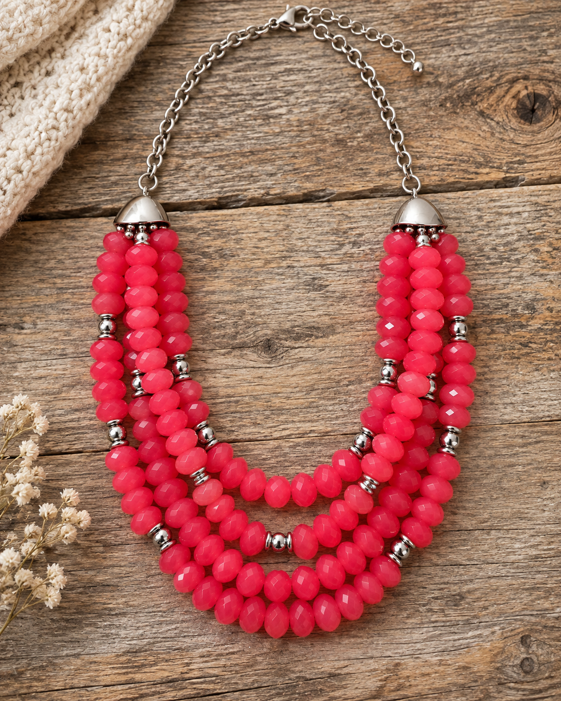 A multi-strand statement necklace featuring vibrant pink faceted beads and silver-toned metal accents, displayed on a rustic wooden surface.