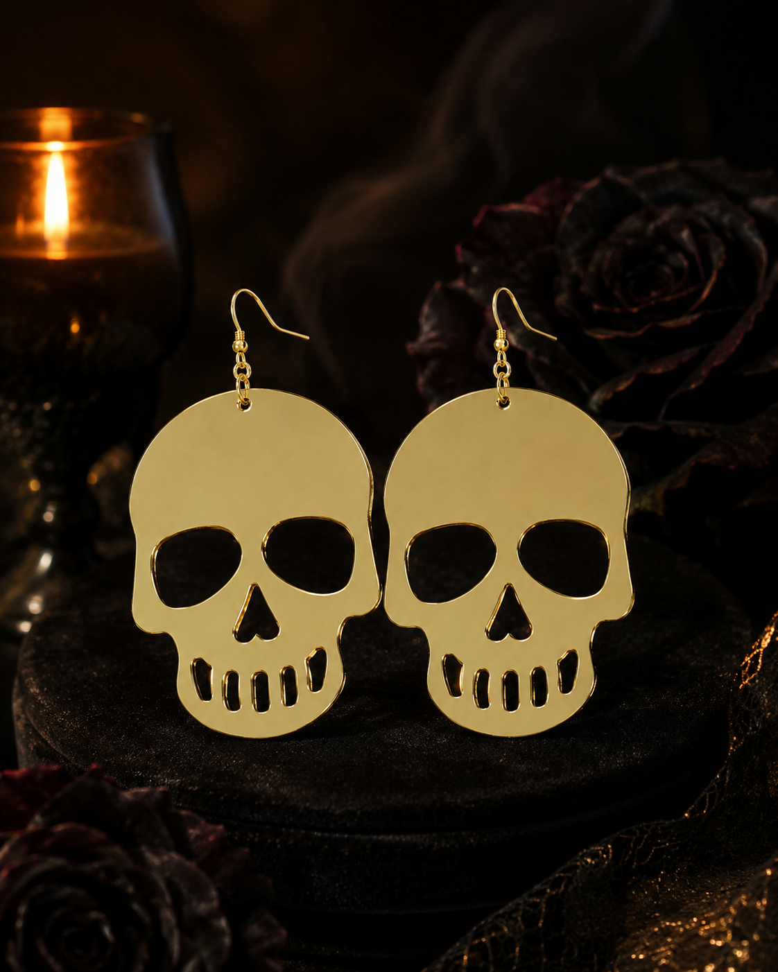 Gold skull Halloween earrings displayed in a moody candlelit setting with dark roses