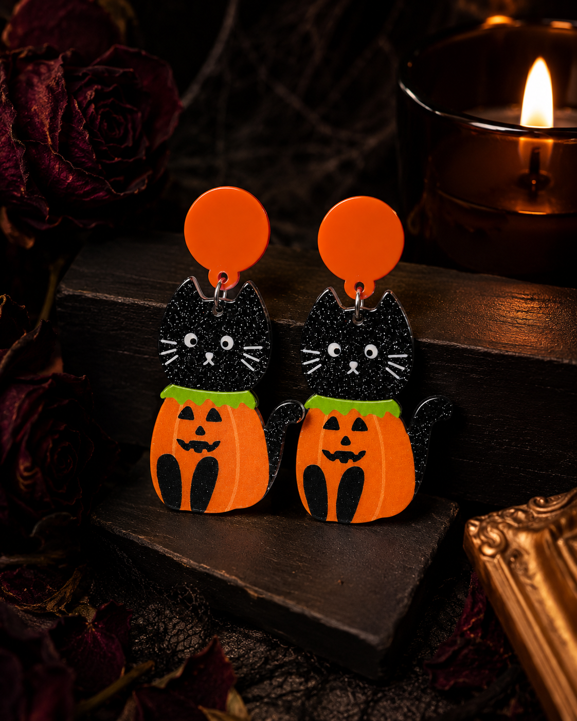 Black cat and pumpkin Halloween earrings displayed in a moody candlelit setting with dark roses