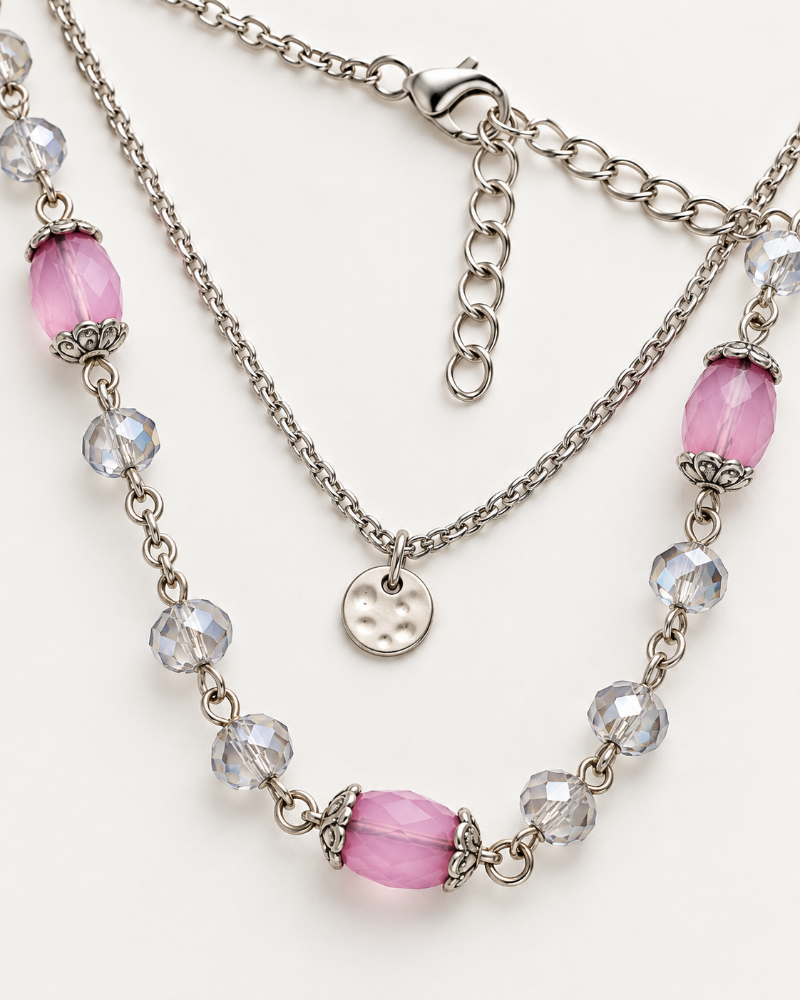 A layered silver-tone necklace featuring a main chain with pink faceted beads, a secondary chain with clear faceted beads, and a small round silver charm, displayed on a clean white background.