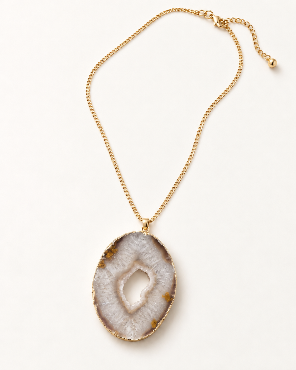 A gold chain necklace featuring a large, irregular-shaped agate slice pendant with a natural geode cavity, displayed on a clean white background.