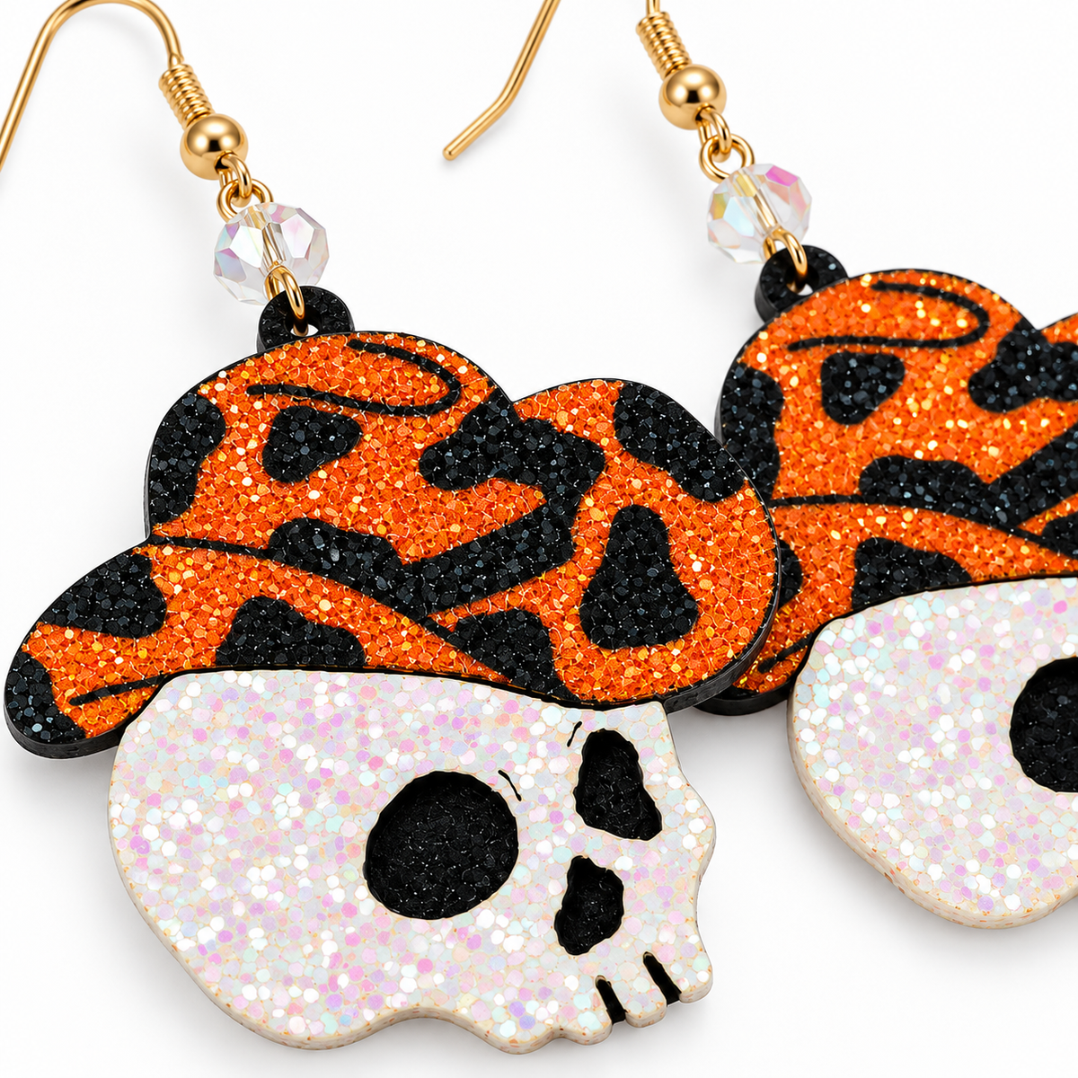Halloween dangle earrings featuring a black and orange glittery witch hat and a white glittery skull charm, suspended from gold hooks with clear faceted beads on a white background.
