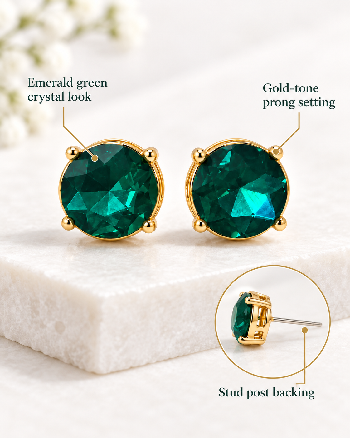 A pair of gold-tone stud earrings with oval emerald green crystal-like fronts, shown on a white stone slab with callout text reading 'Emerald green crystal look' and 'Gold-tone prong setting,' plus a circular inset showing the stud post backing.