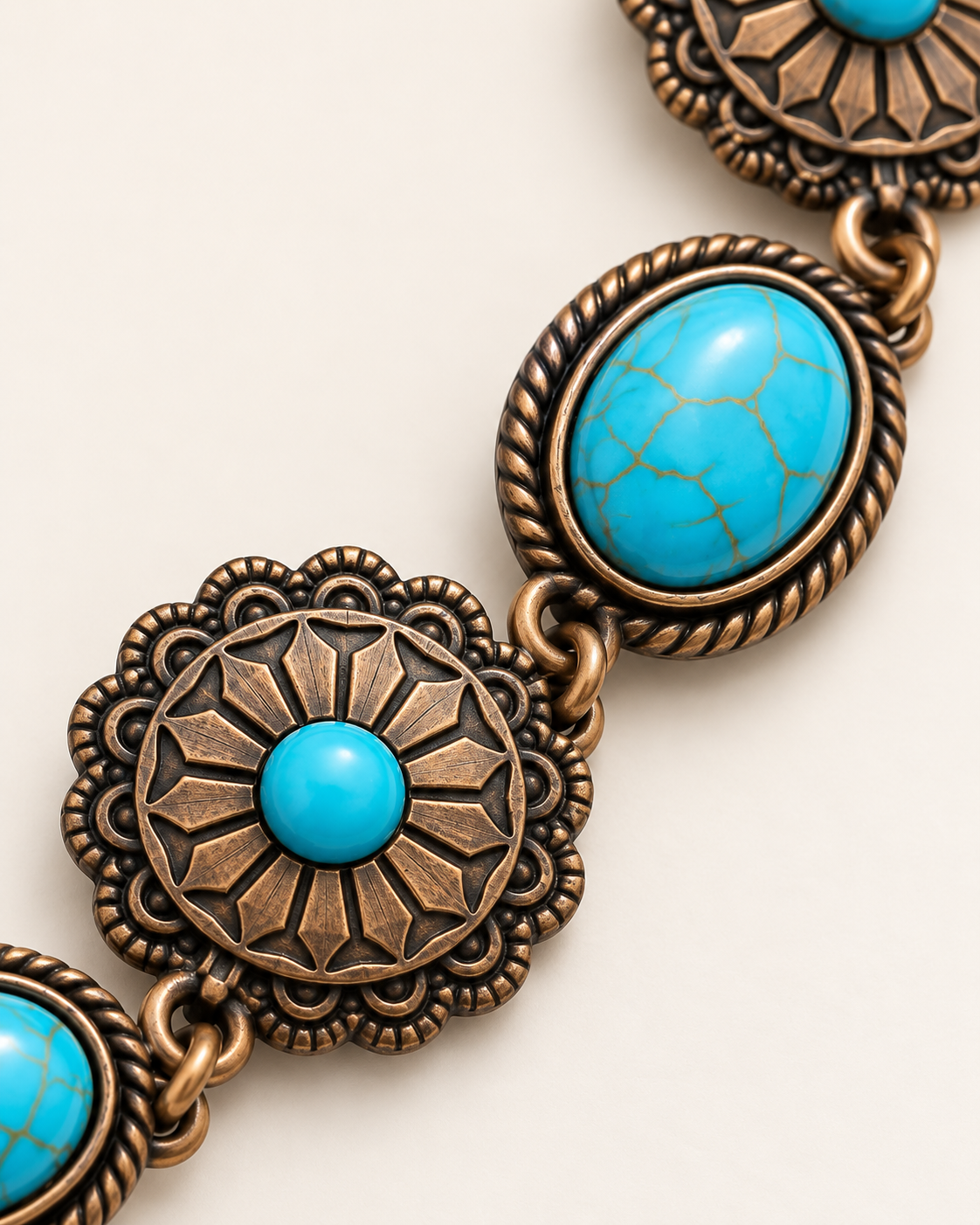 Close-up of an ornate bracelet featuring oval turquoise stones and circular bronze-toned medallions with floral detailing, set against a light beige background.