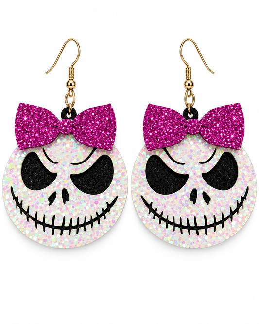 A pair of dangling earrings shaped like Jack Skellington's face, featuring a glittery pink bow on a white glittery circular face with black facial details and gold fishhook wires.
