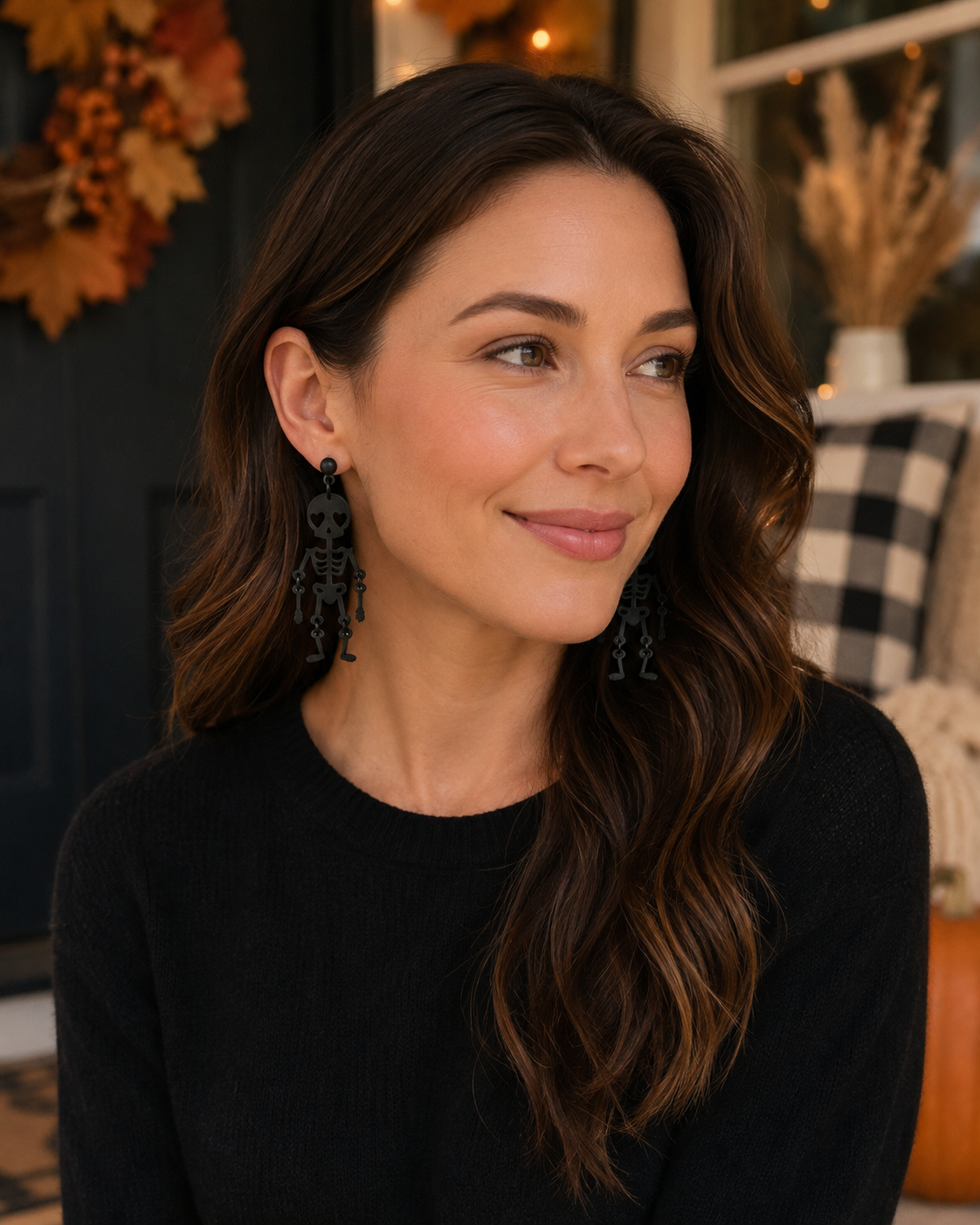 Woman wearing Love You to Death skeleton earrings with a black top in a warm fall setting