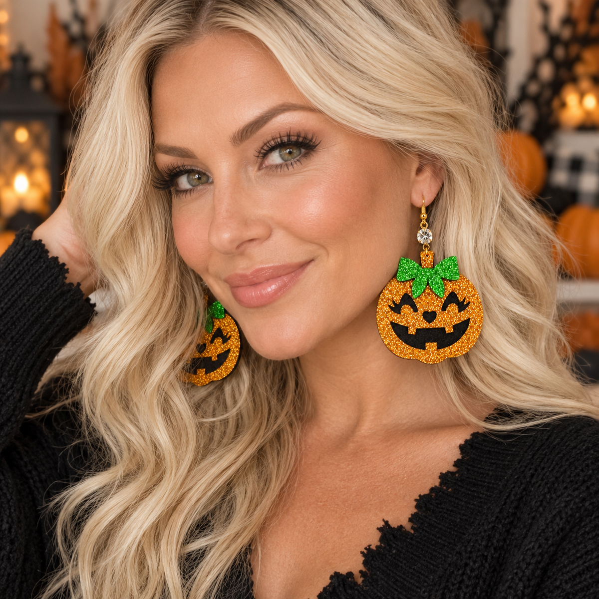 A close-up lifestyle shot of a blonde woman wearing large, orange and green beaded jack-o'-lantern dangle earrings with a rhinestone accent, set against a warm, Halloween-themed background.