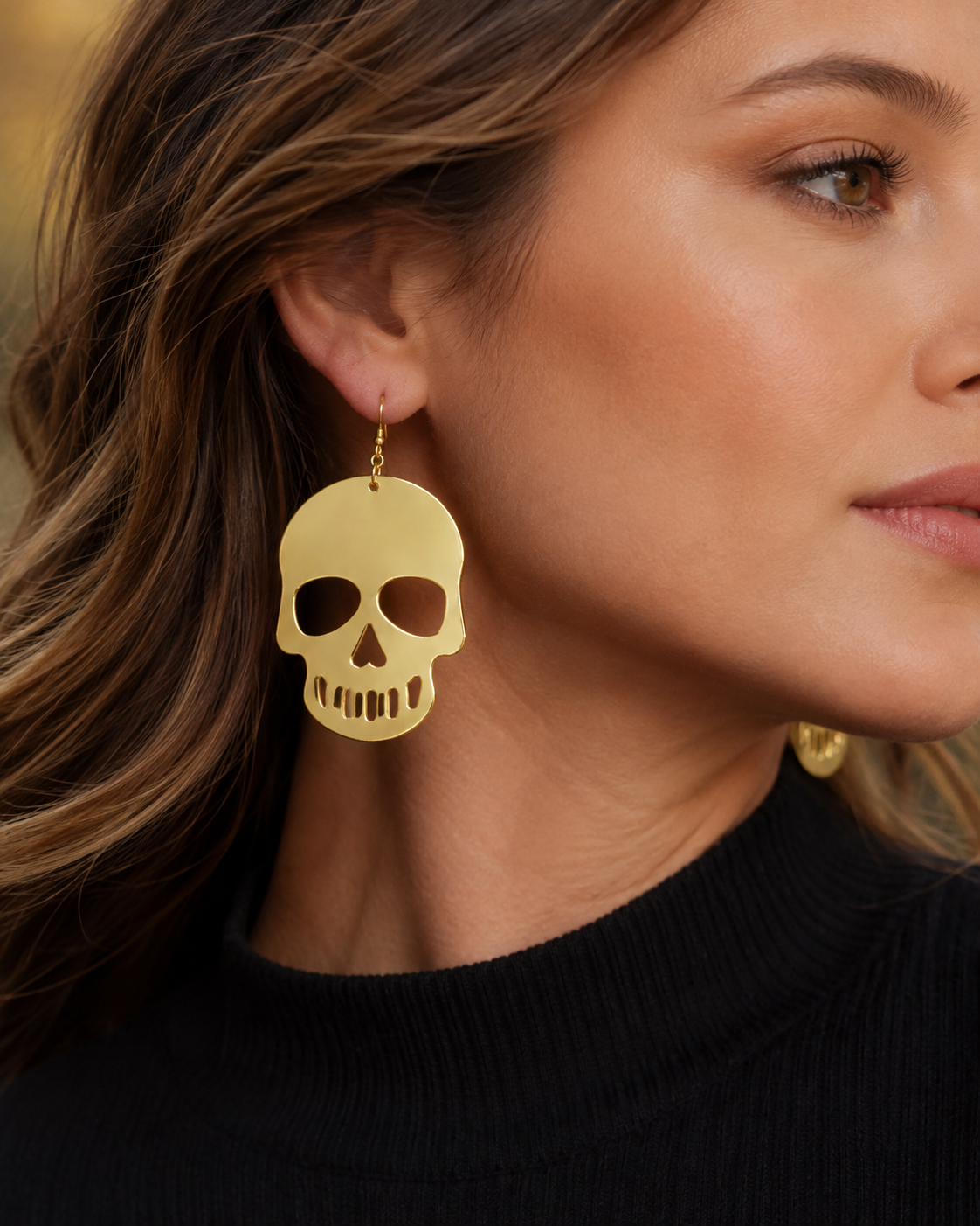 Woman wearing oversized Gilded Afterlife gold skull statement earrings with a black top