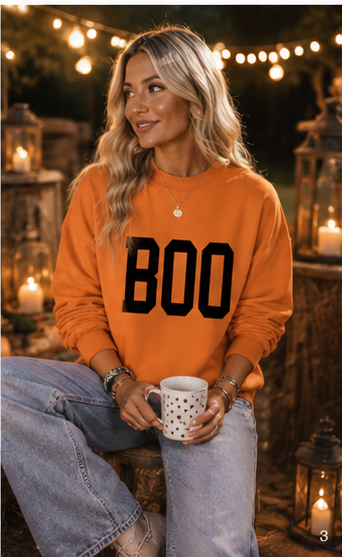 Emma wearing the Double the Boo Reversible Sweatshirt in a warm After Dark evening setting with glowing lights and pumpkins.