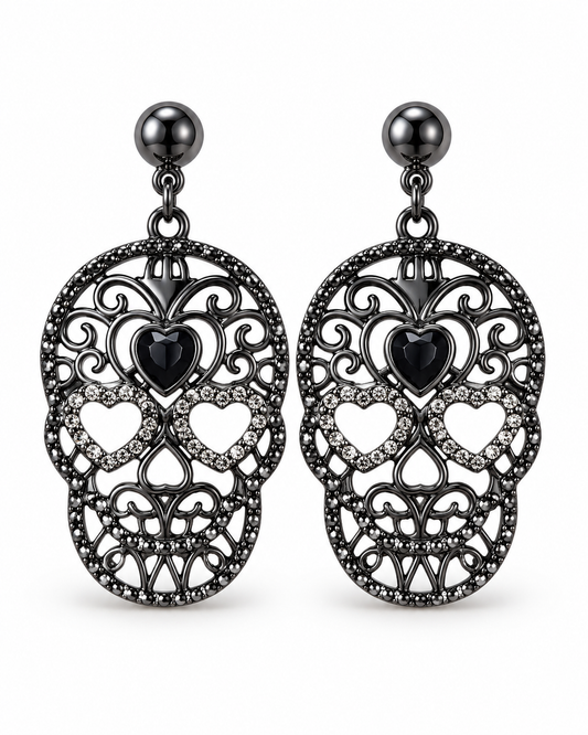 A pair of gothic-style drop earrings featuring intricate filigree sugar skull designs in black metal, adorned with small clear rhinestones and a central black heart-shaped stone, suspended from dark metallic ball studs.