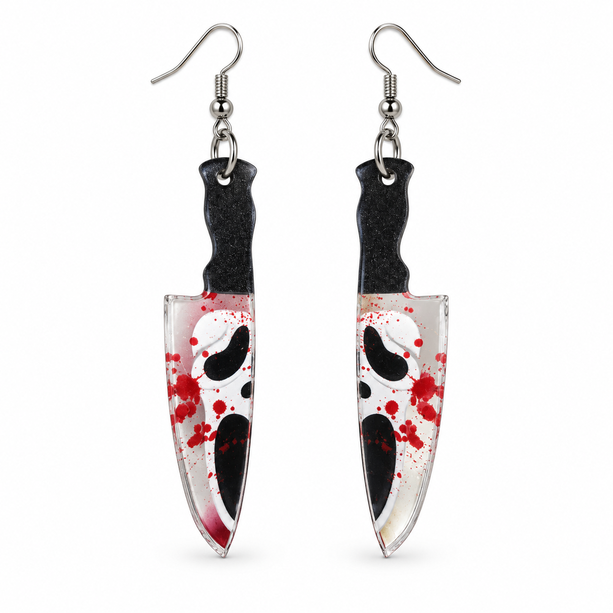 A pair of dangling earrings shaped like knives, featuring a white and black Ghostface mask design with red blood splatter, suspended from silver fishhook wires on a plain white background.