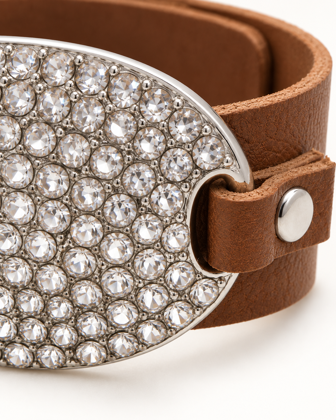 A close-up of a brown leather belt featuring a large, oval silver-tone buckle embellished with clear rhinestones, set against a plain white background.