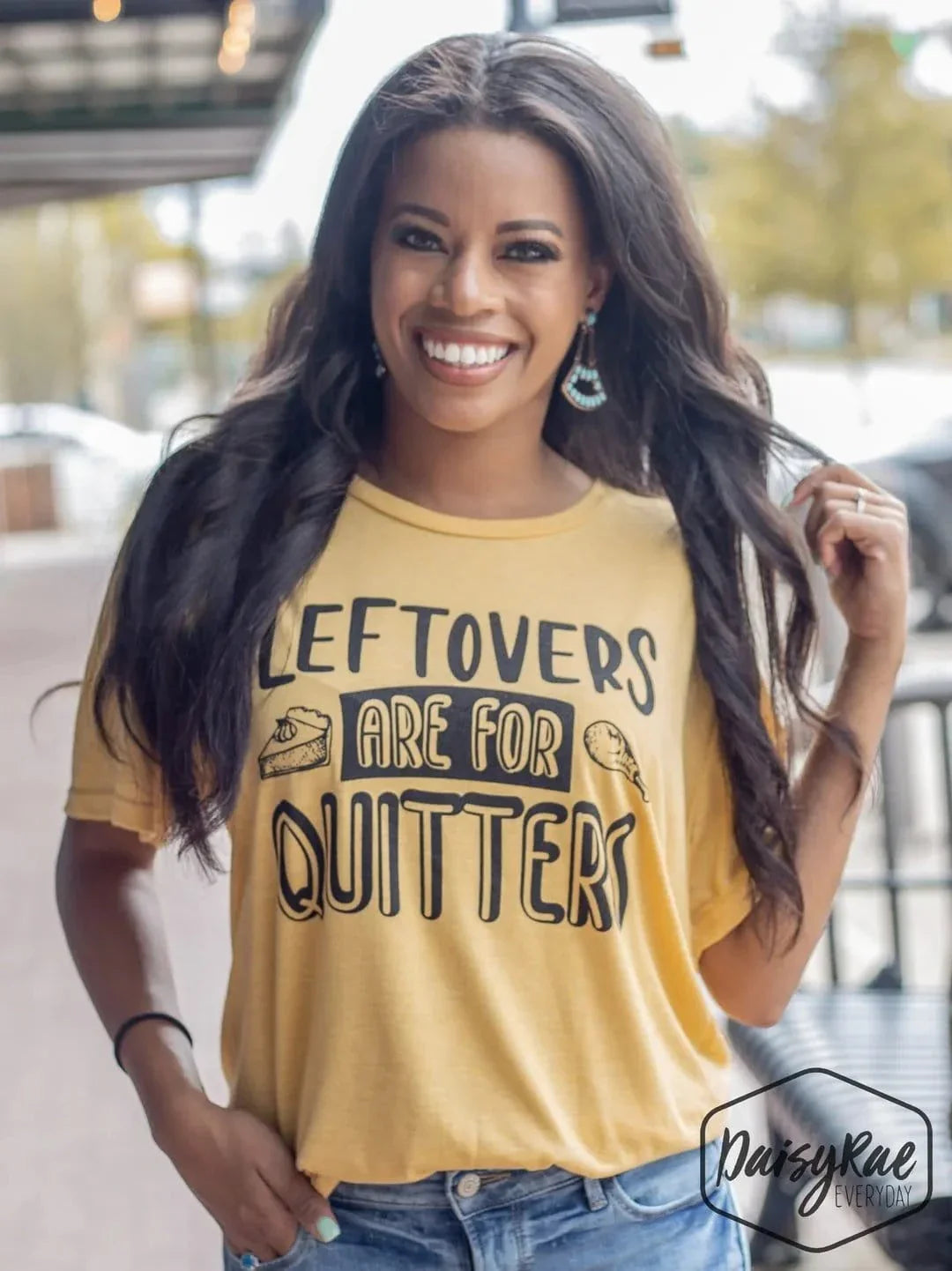 Woman wearing a yellow "Leftovers Are for Quitters" Thanksgiving graphic tee smiling outdoors